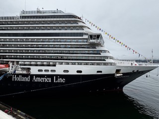Holland America Line cruise ship docked at port with multiple decks visible against a gray sky