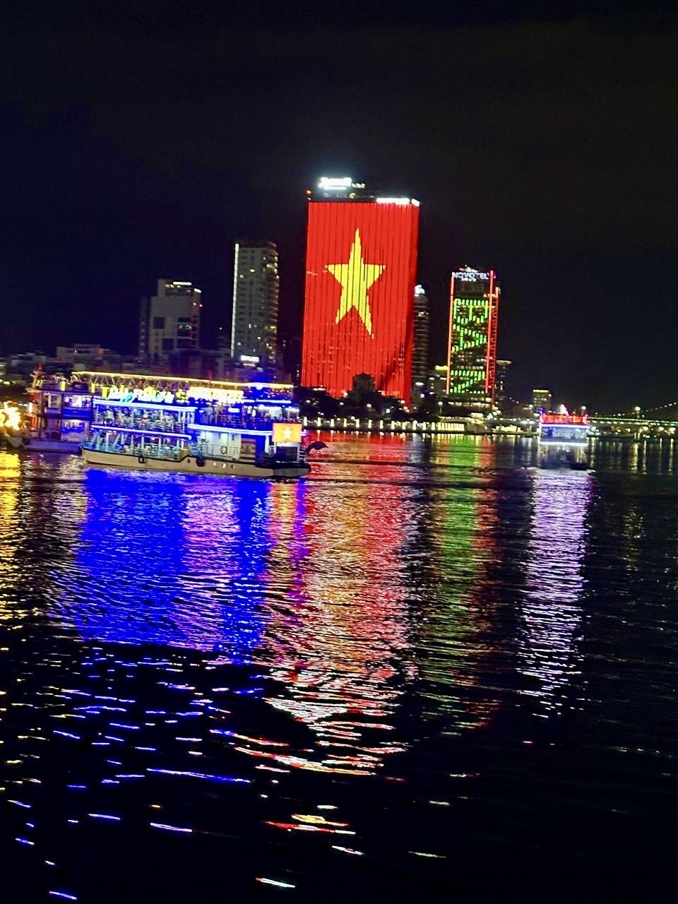 Da Nang cityscape at night with illuminated buildings reflected in the Han River and a tour boat