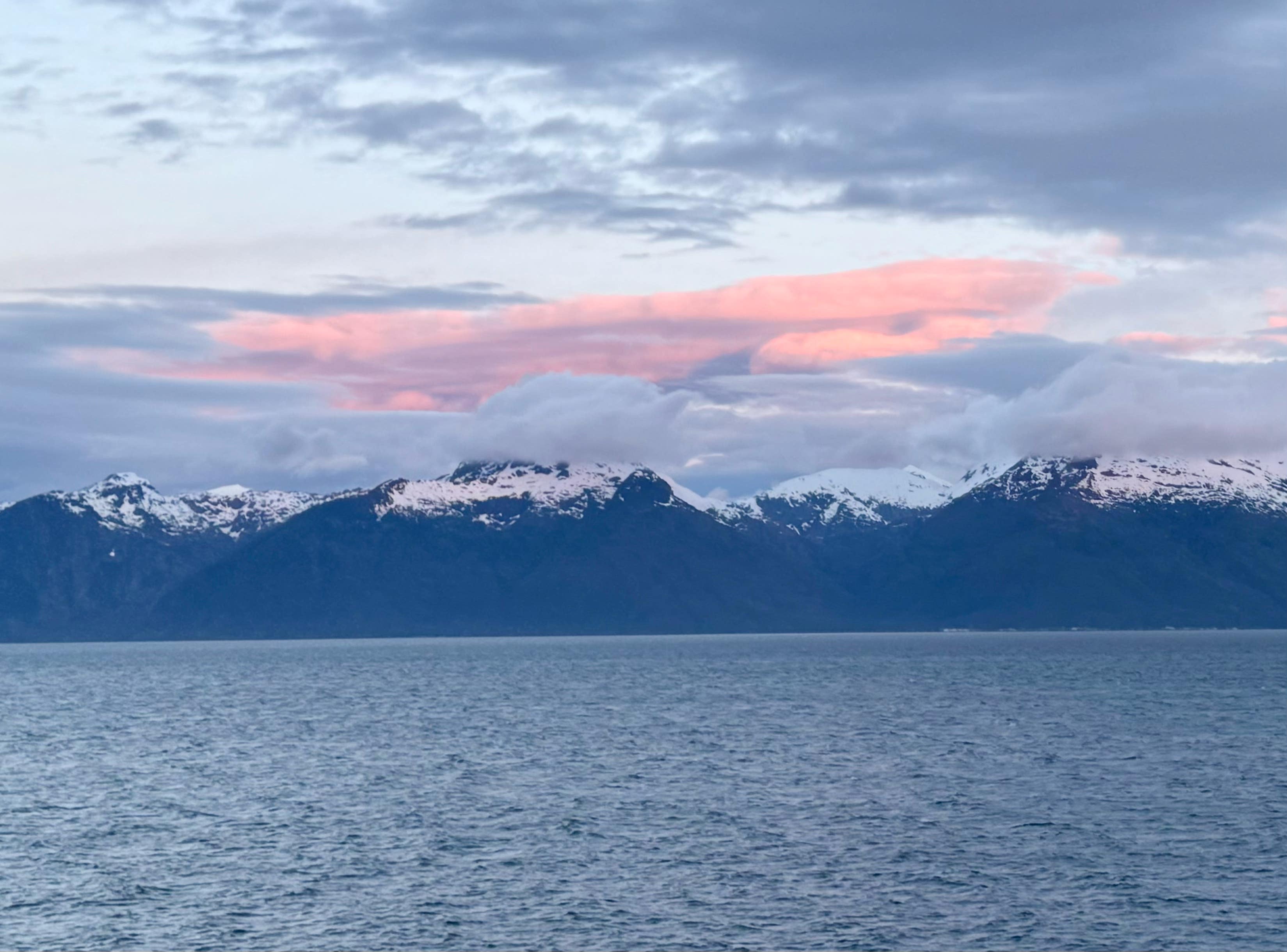 Snow-capped coastal mountains glow beneath a vivid pink sunset sky reflected over calm arctic waters.