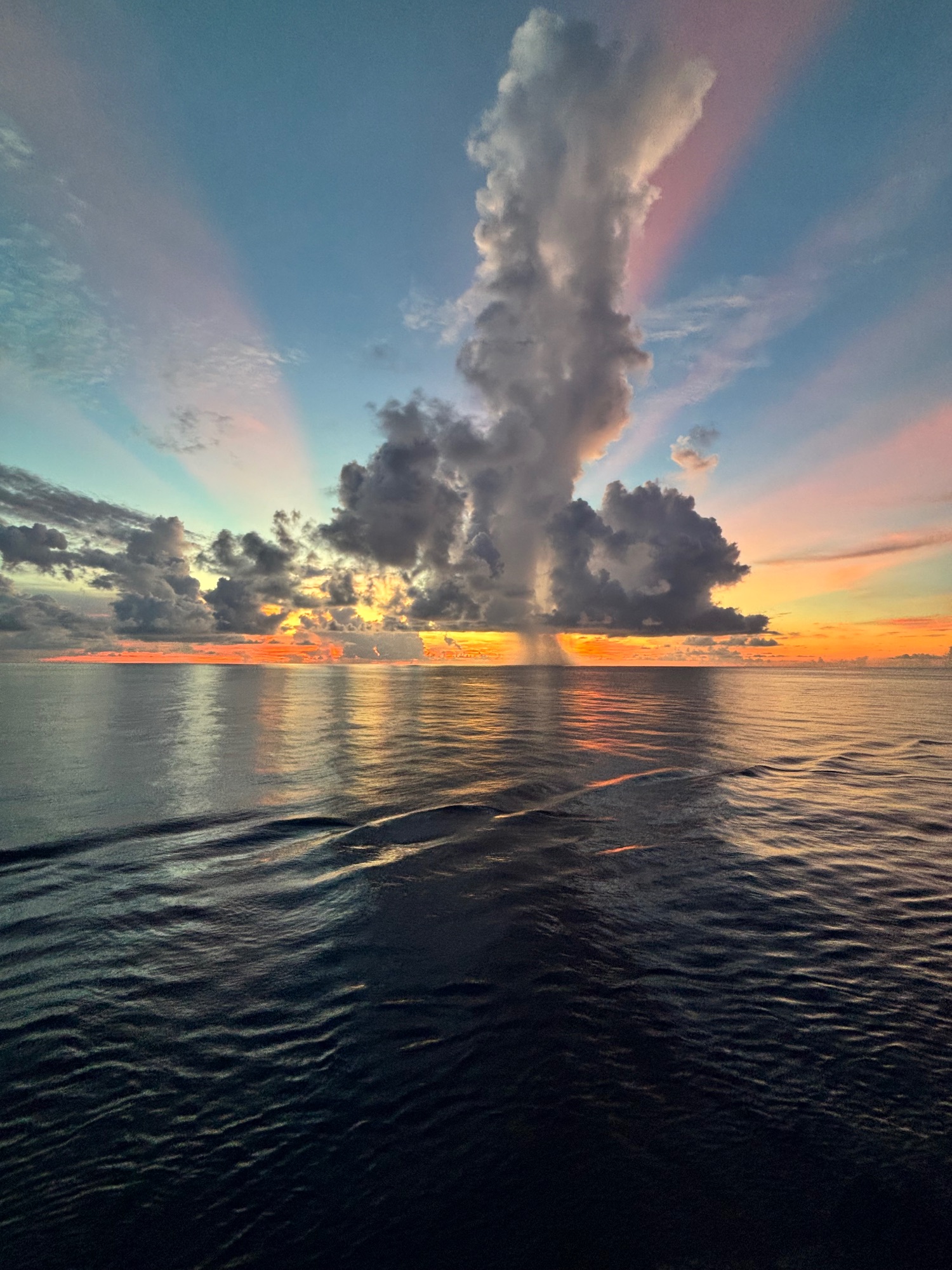 Dramatic sunset over calm ocean with towering clouds illuminated in orange and pink, reflecting on dark water