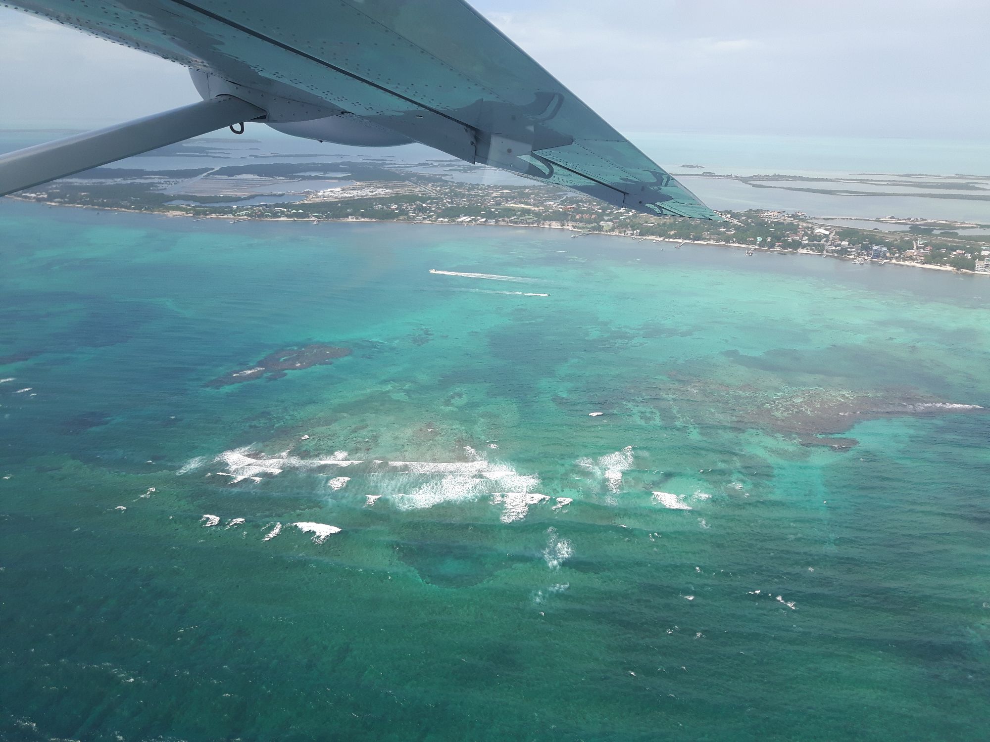 Aerial view from small aircraft showing turquoise Caribbean waters, reef formations, and coastal settlement