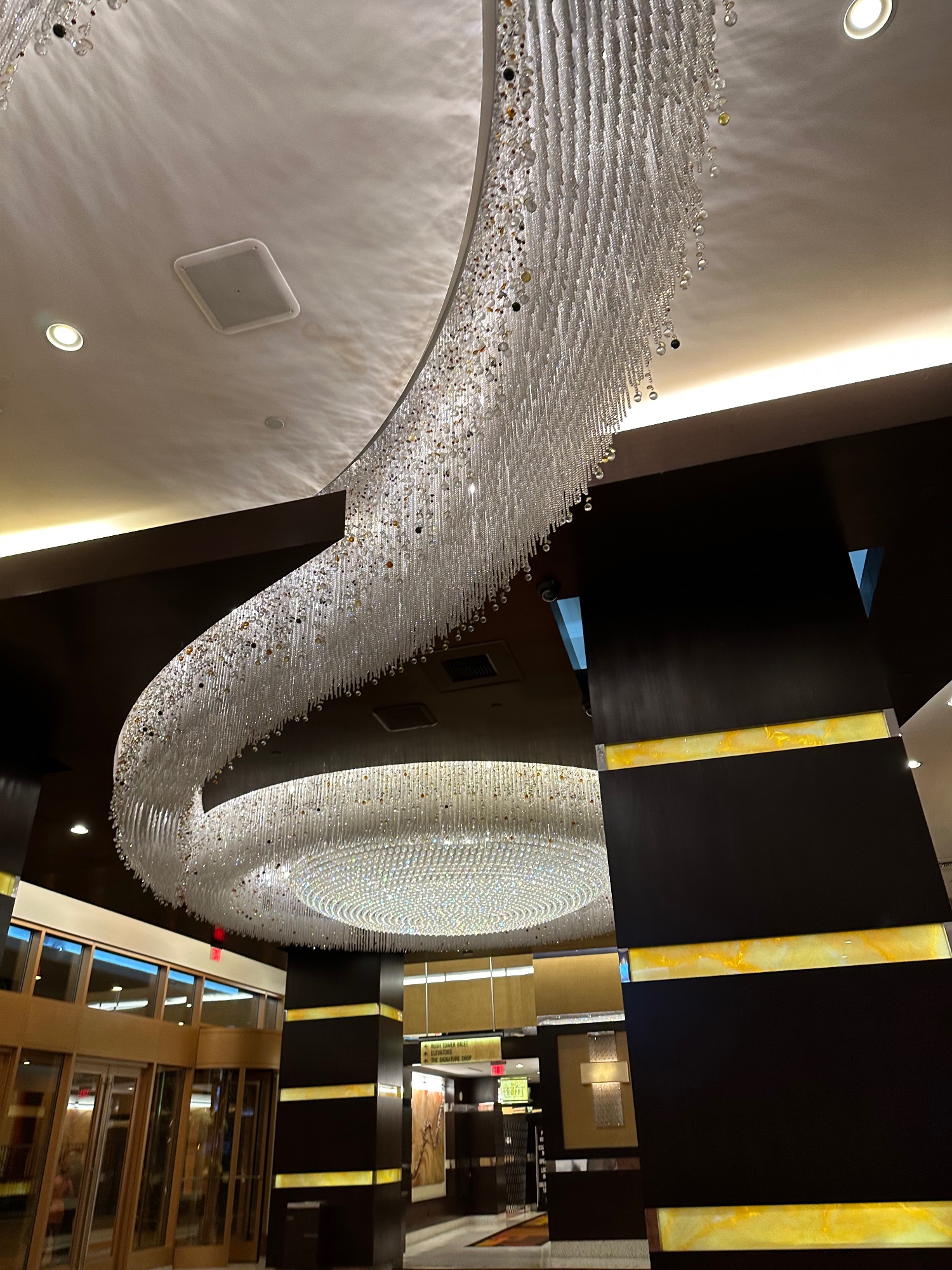 Spiral crystal chandelier installation in modern hotel lobby with curved architectural elements and recessed lighting