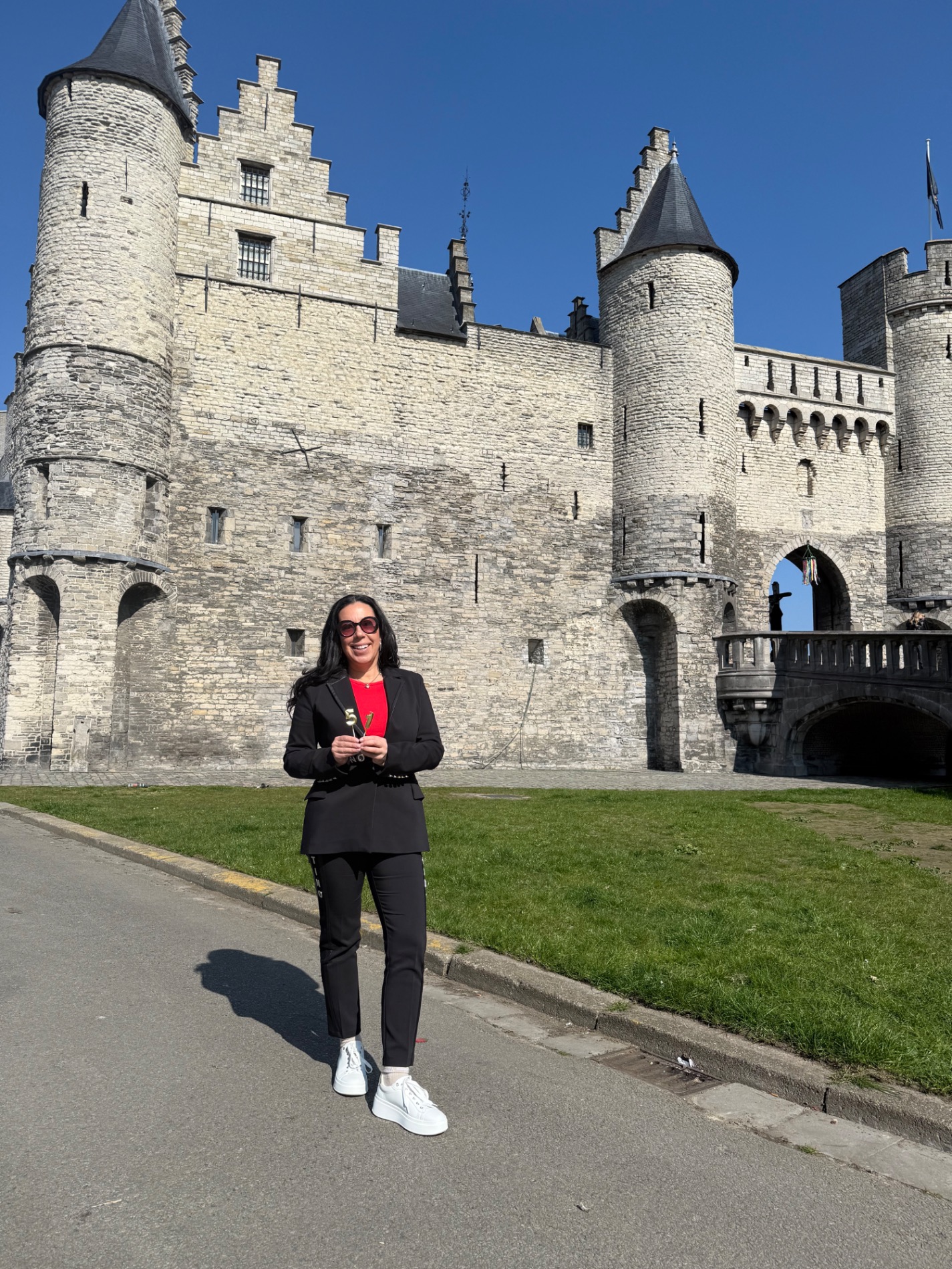 Woman in black blazer and red shirt standing in front of stone castle with towers