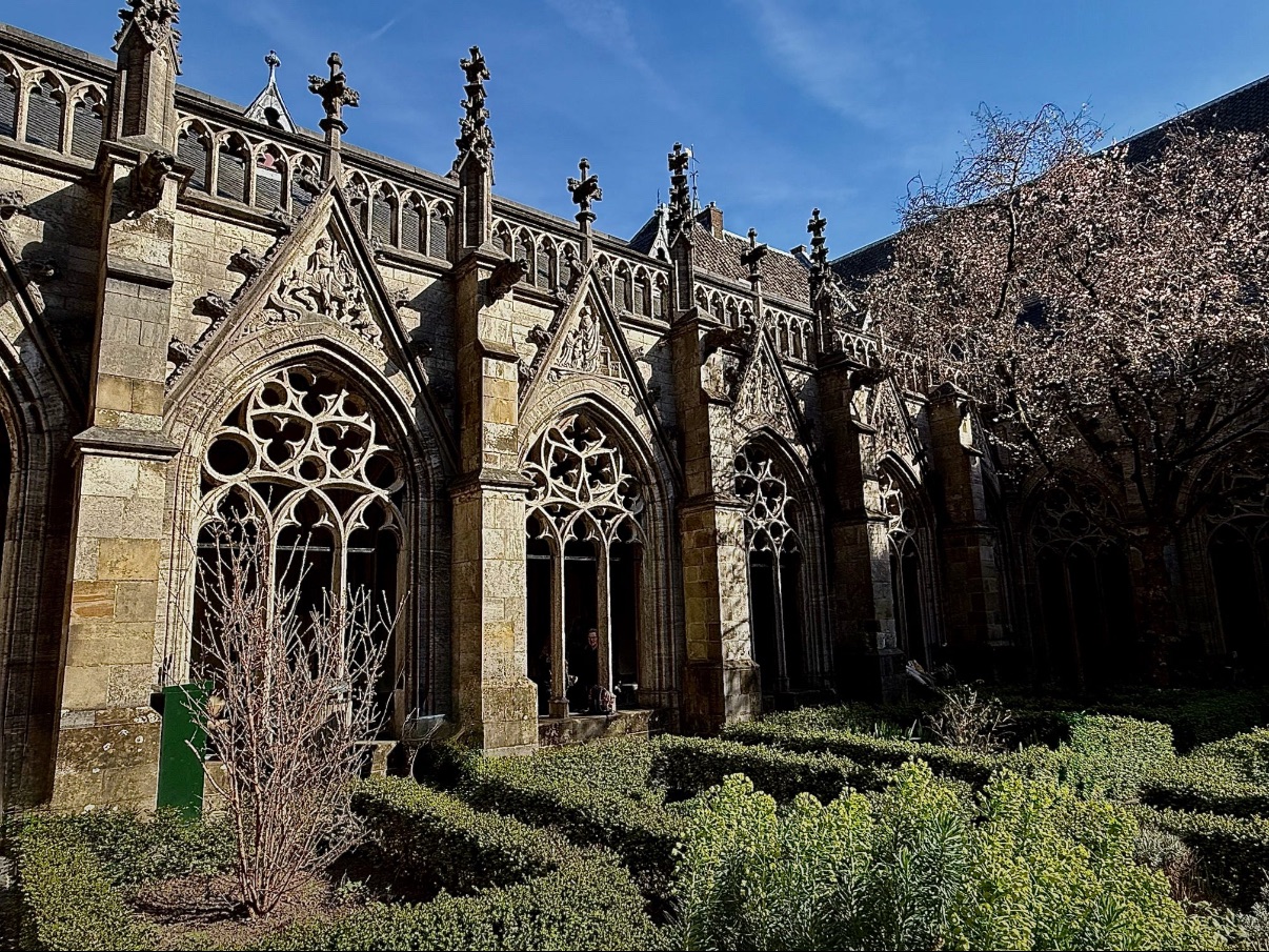 Gothic church cloister with ornate stone arches and manicured hedges in courtyard
