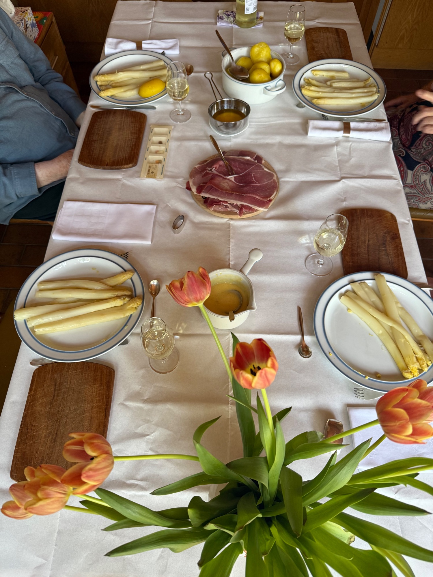 Elegant dining table set with white linens, white asparagus plates, prosciutto, lemons, and tulip centerpieces