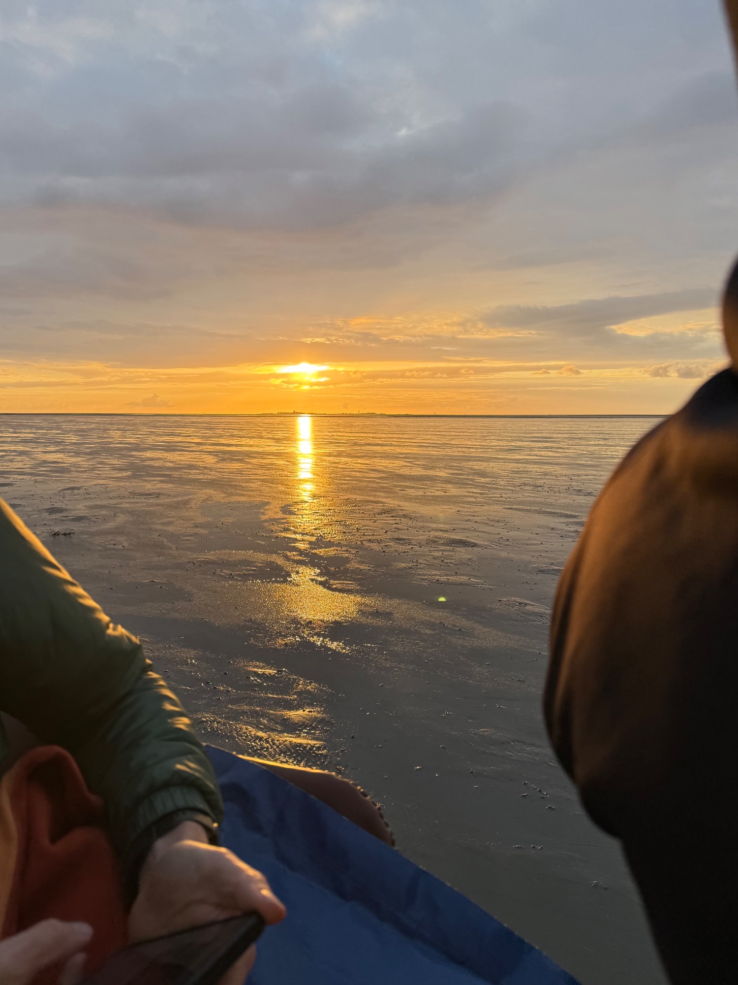Sunset over shallow tidal flats with golden light reflecting on water, viewed from a boat
