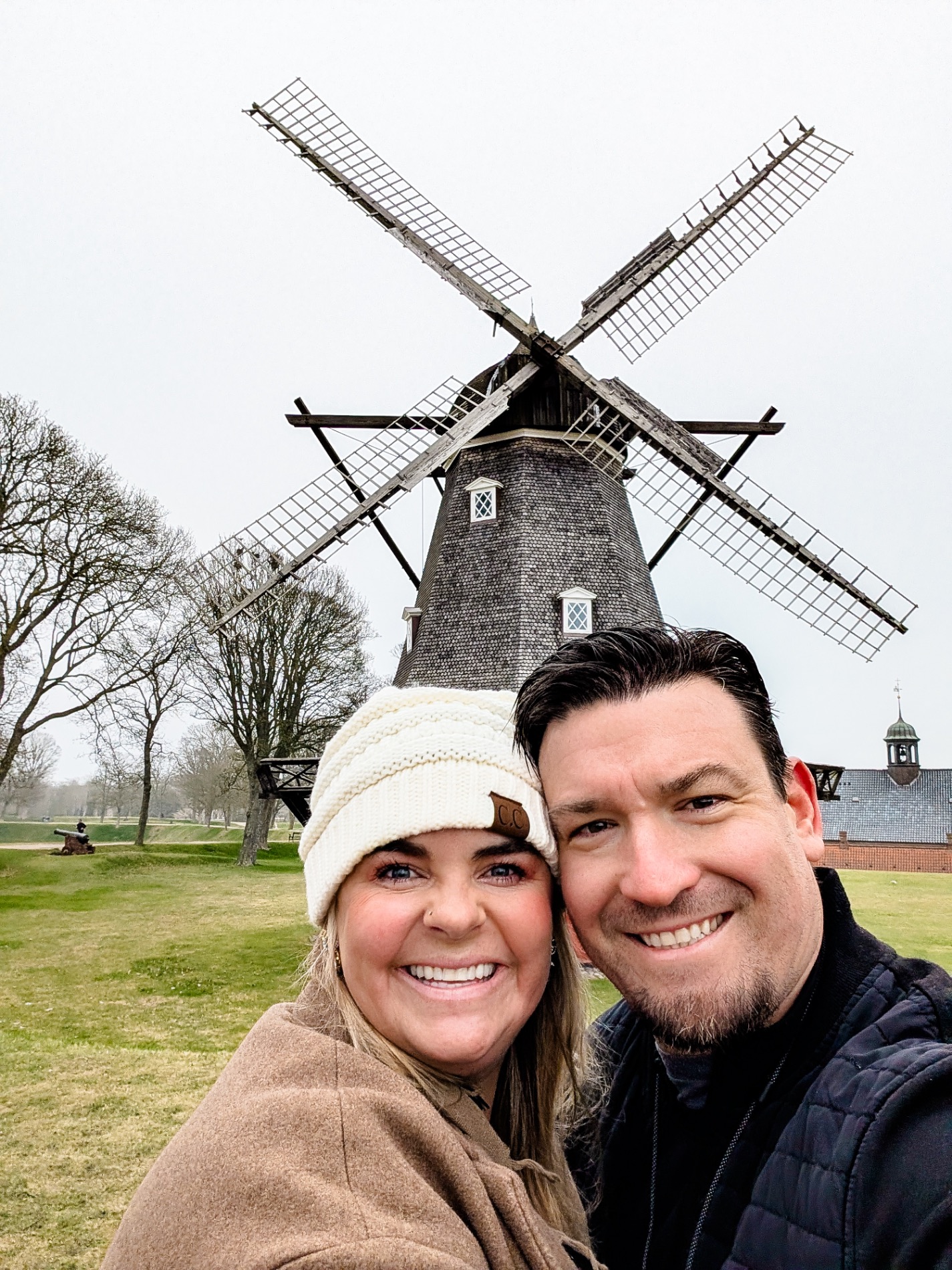 Traditional Dutch windmill with large rotating blades in a grassy field with bare trees