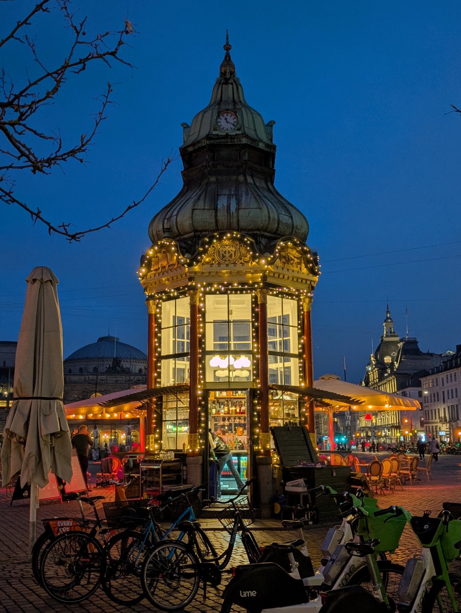 Illuminated historic clock tower pavilion at night with bicycles parked nearby in a European city square