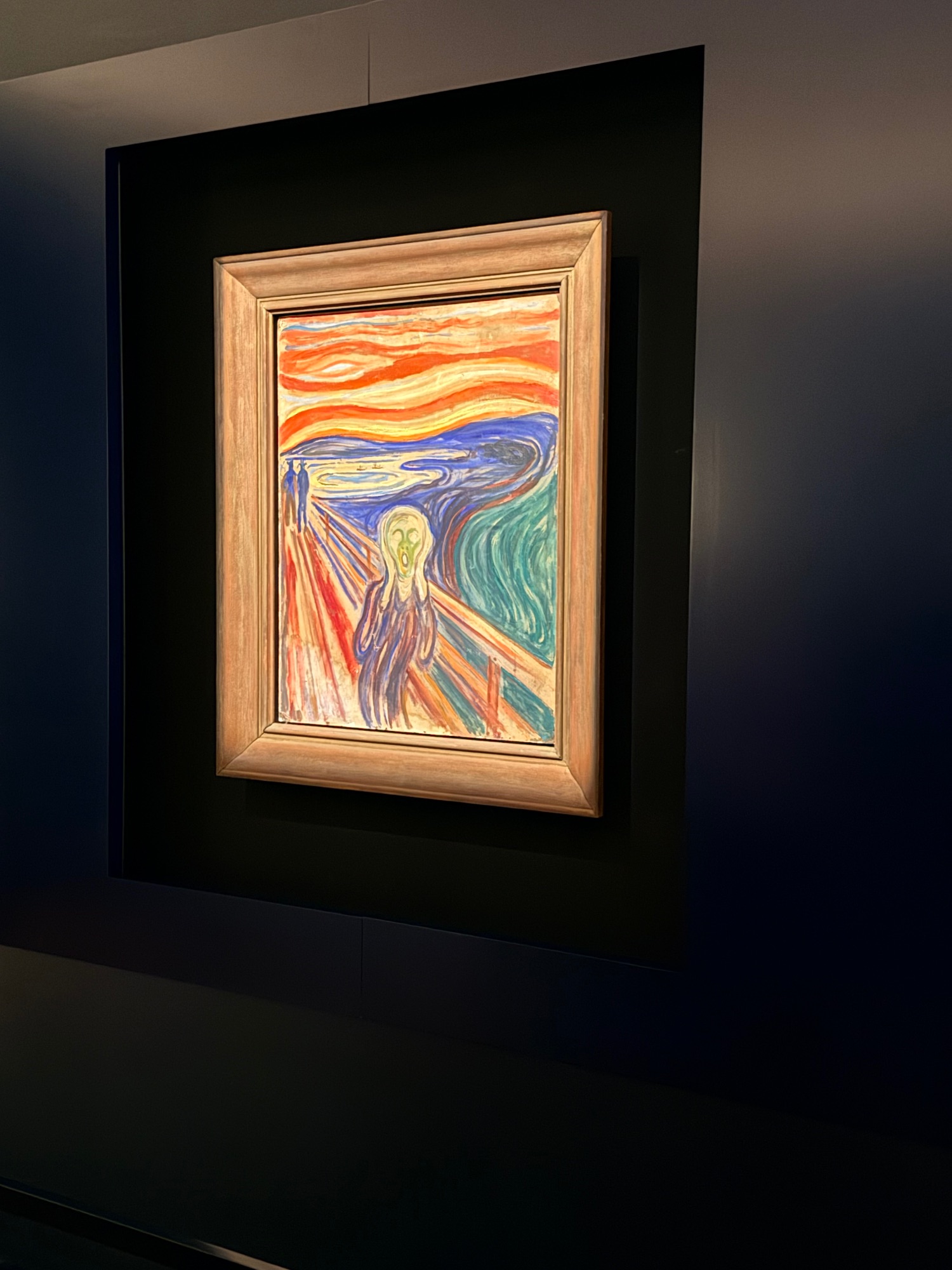 Edvard Munch's The Scream painting displayed in a wooden frame against a black gallery wall