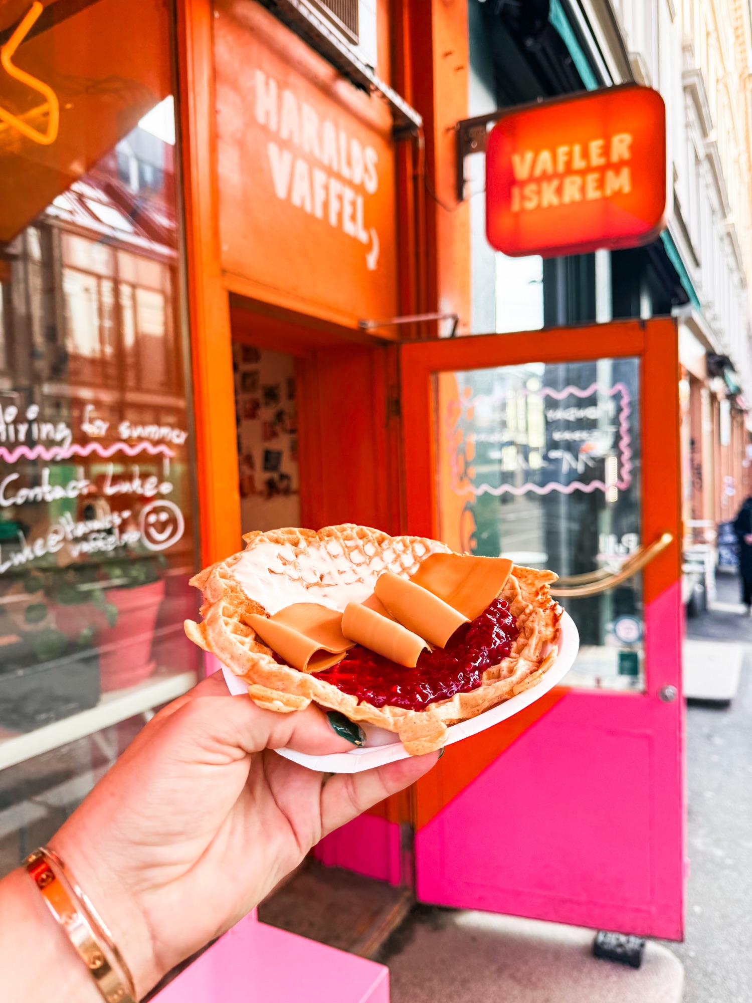 Hand holding a Danish waffle cone with jam and rolled waffle cookies in front of a bright orange storefront in Copenhagen