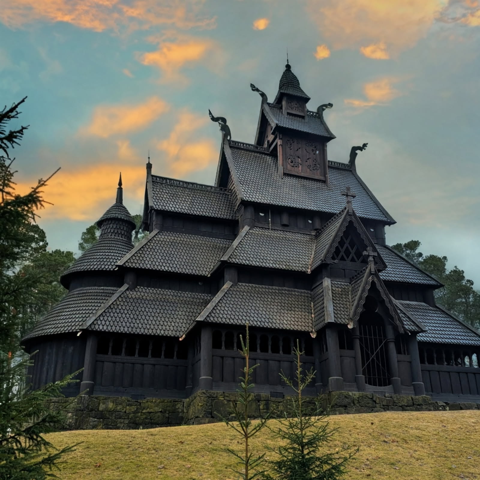 Stave church with multiple black wooden tiered roofs and ornate dragon-head decorations against a cloudy sky