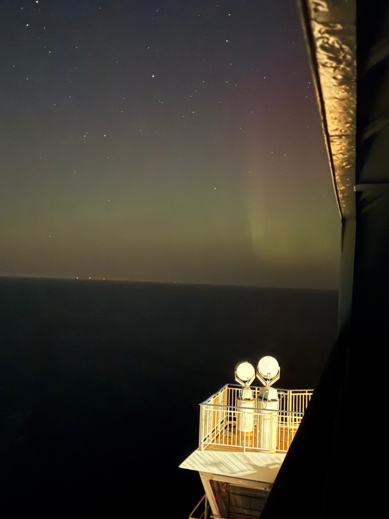 Starry night sky above a wooden cabin balcony with illuminated railings overlooking dark water