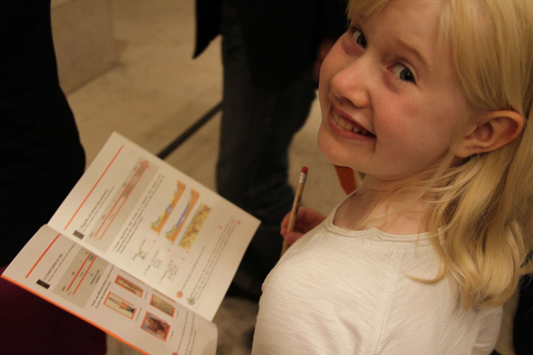 A young blonde child smiles while holding an educational worksheet with diagrams and illustrations