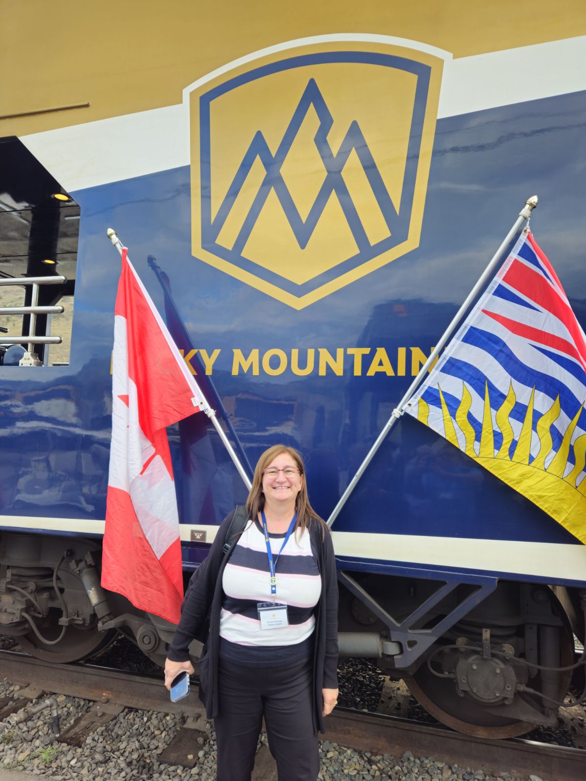 Donna posing in front of a Rocky Mountaineer train car with Canadian and British Columbia flags
