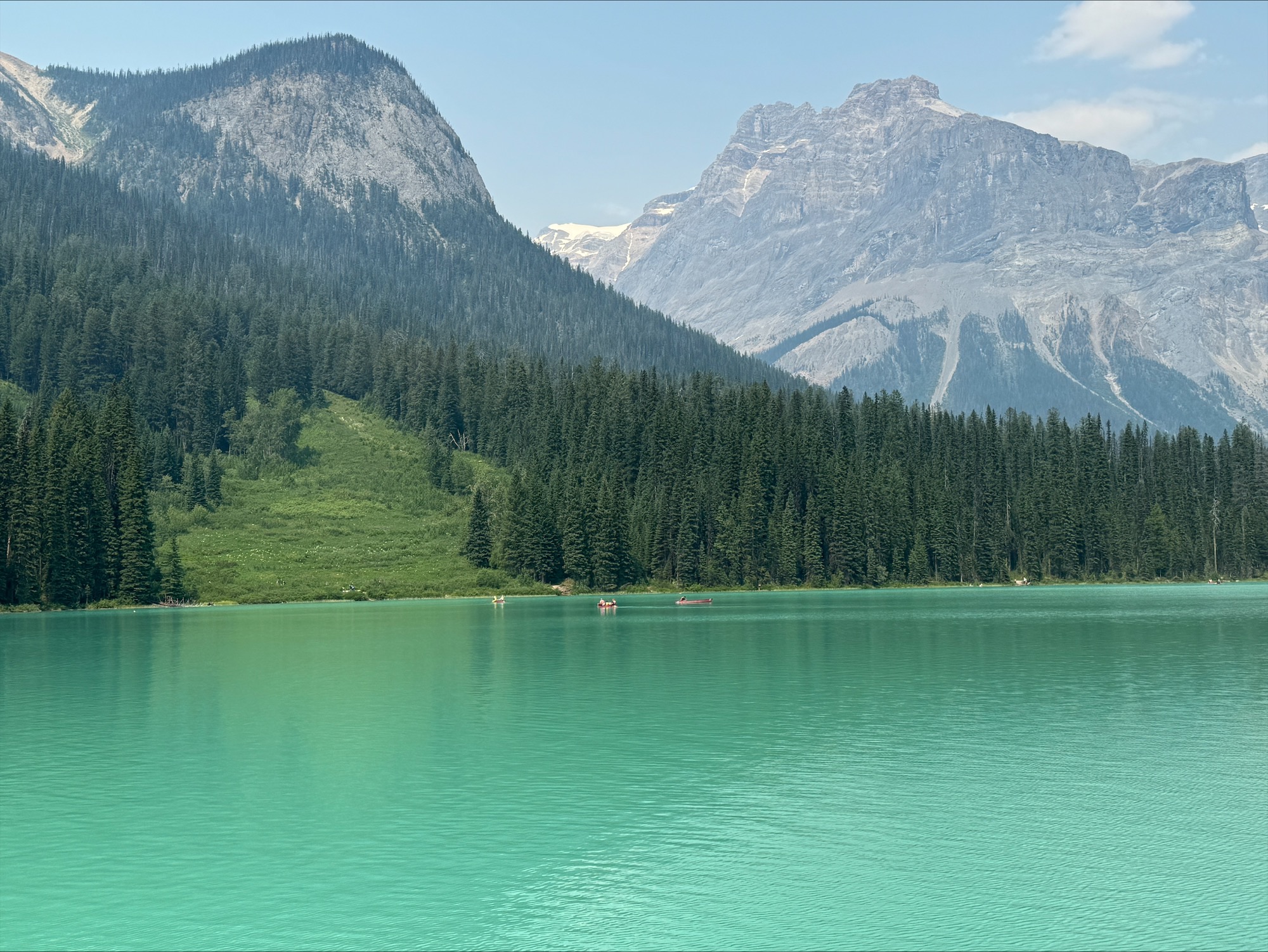 Emerald-green lake nestled between tall mountains with forest-covered slopes and rocky shoreline