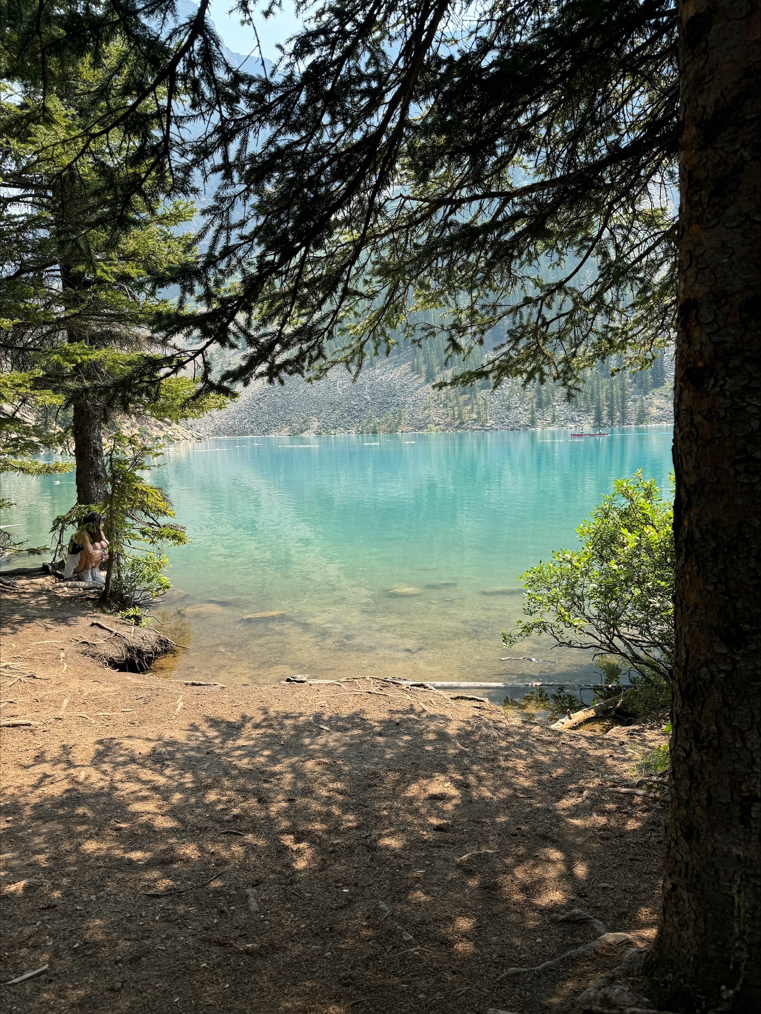 Donna sitting on a stone wall at the edge of a turquoise lake with dramatic mountain peaks behind her