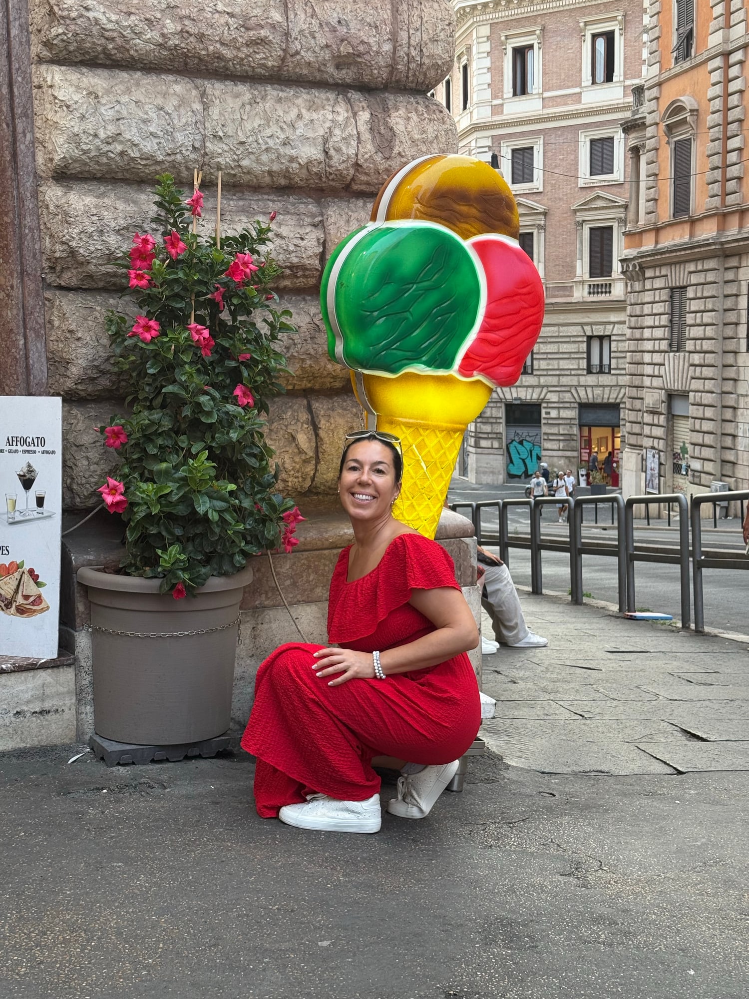 Katia crouches beside a large colorful Italian ice cream cone sculpture on a Rome street