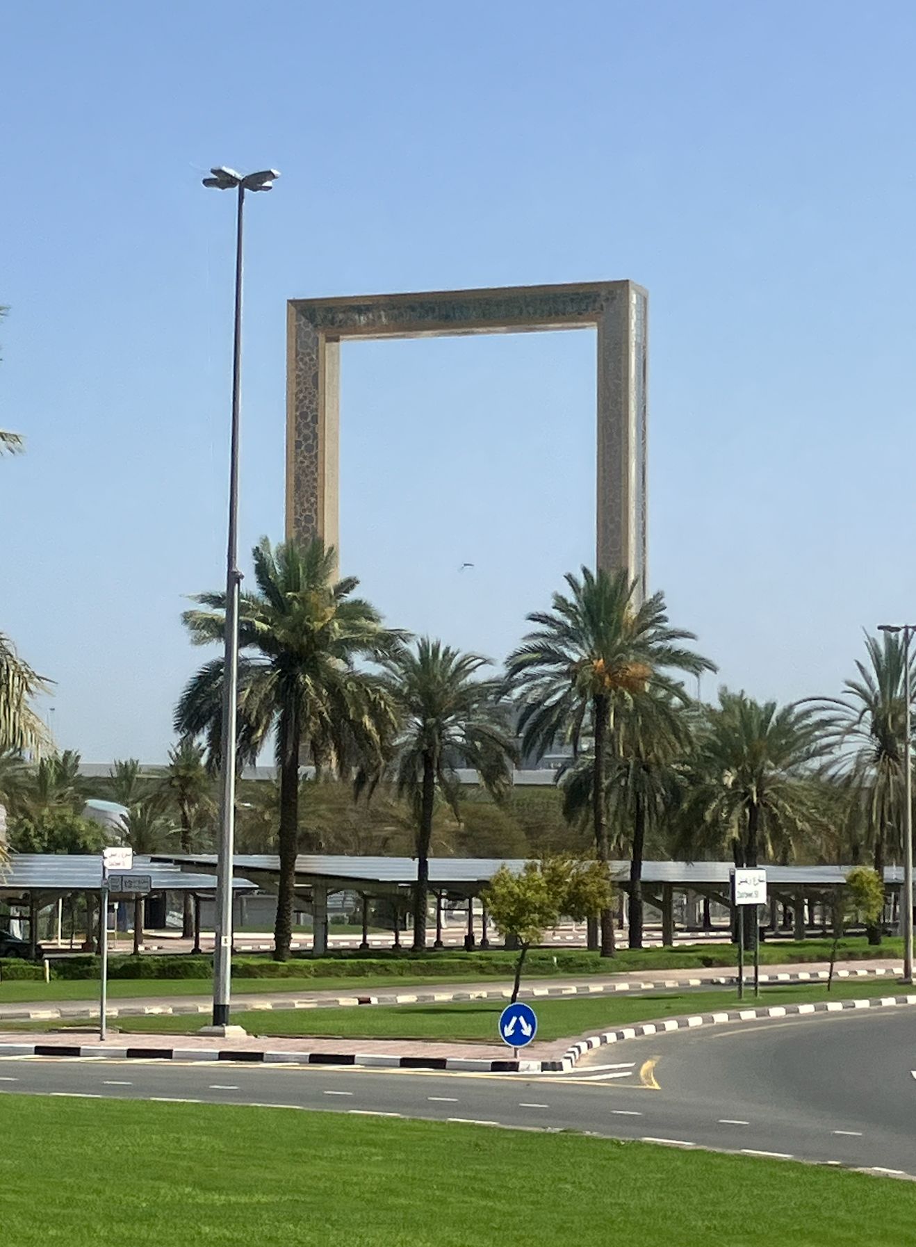 Large concrete picture frame structure surrounded by palm trees on a manicured green median in Dubai