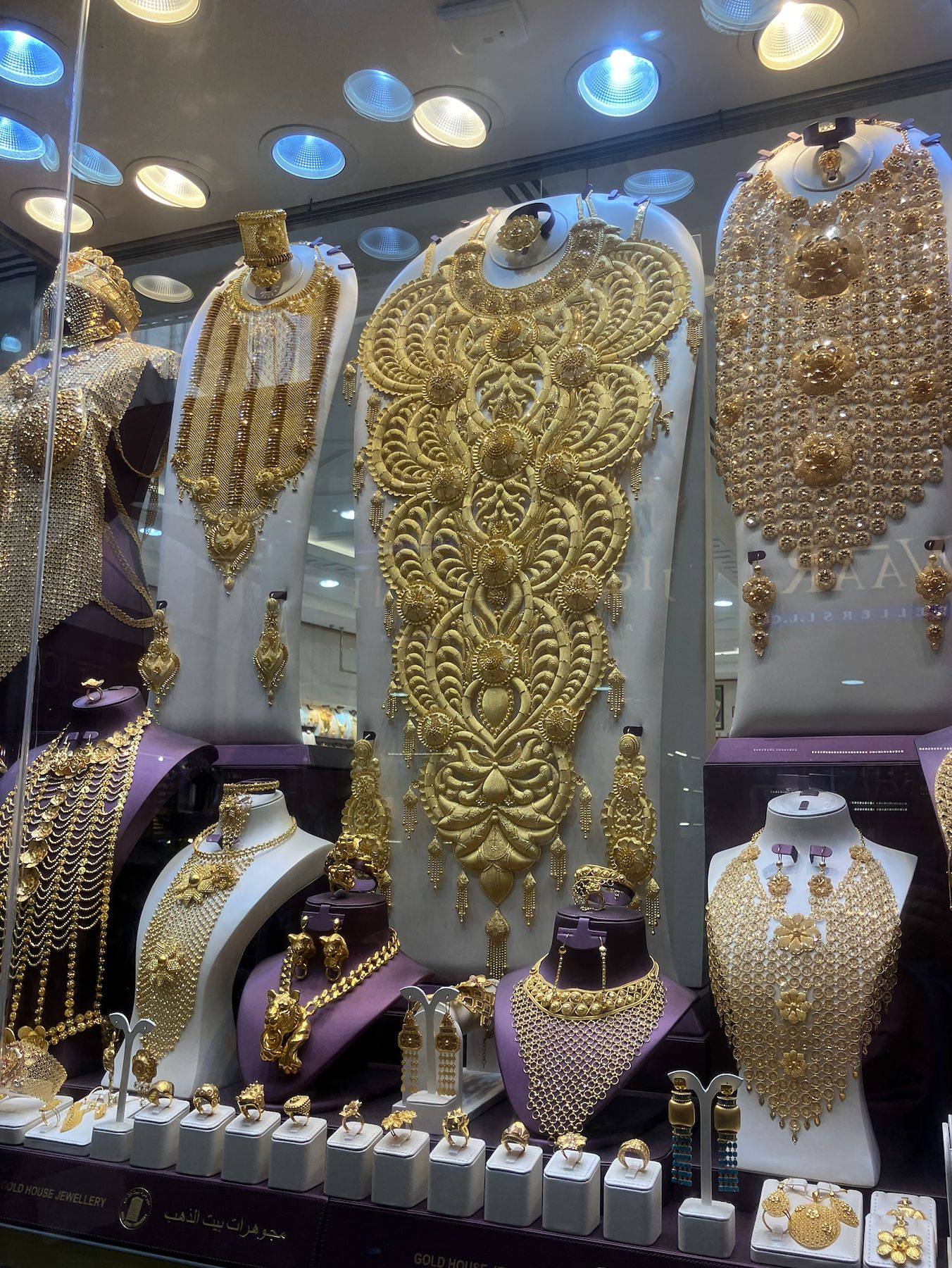 Ornate gold jewelry display in a shop window featuring elaborate necklaces and traditional Gulf-style accessories