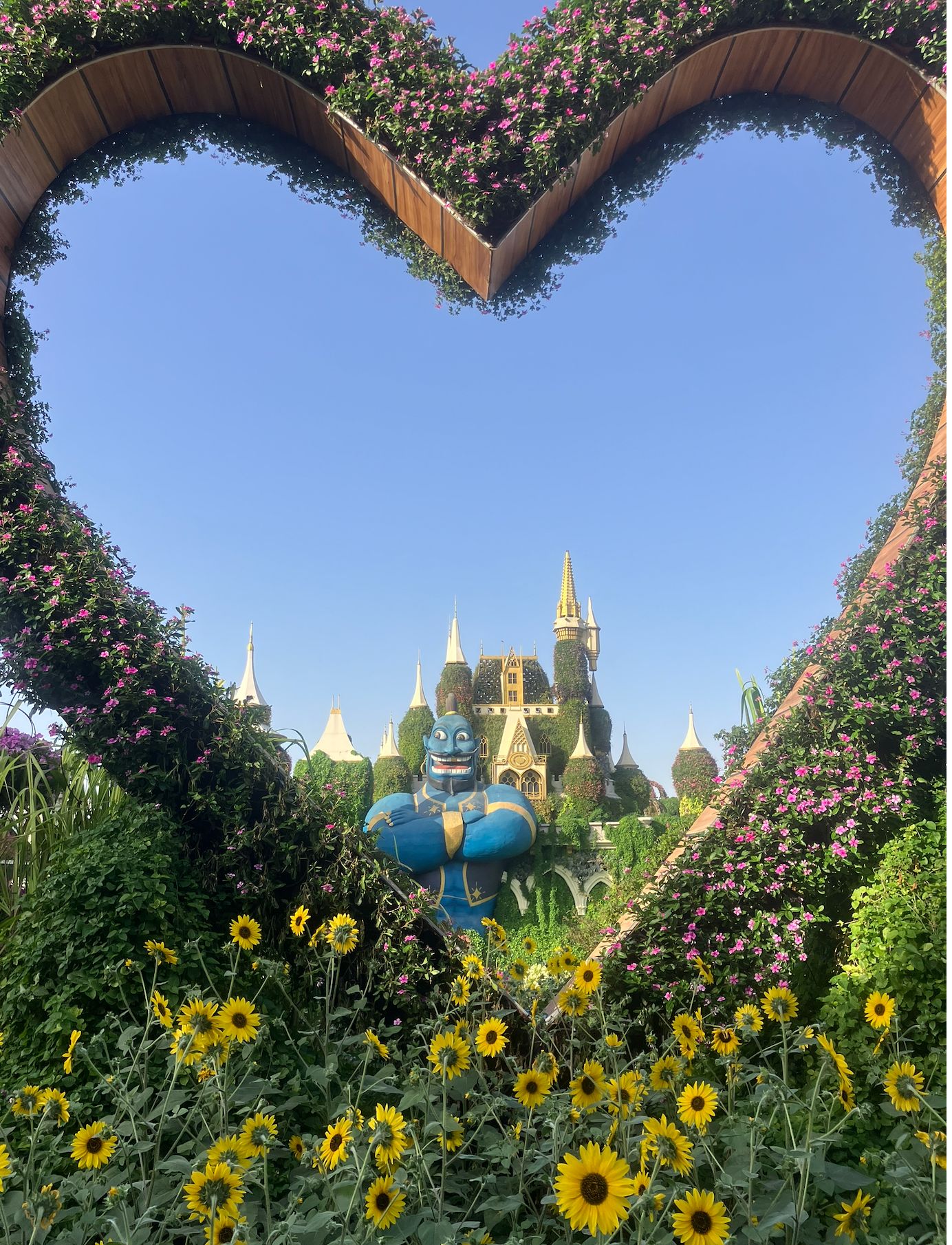 Heart-shaped floral arch framing a castle and blue character figure with sunflowers in foreground