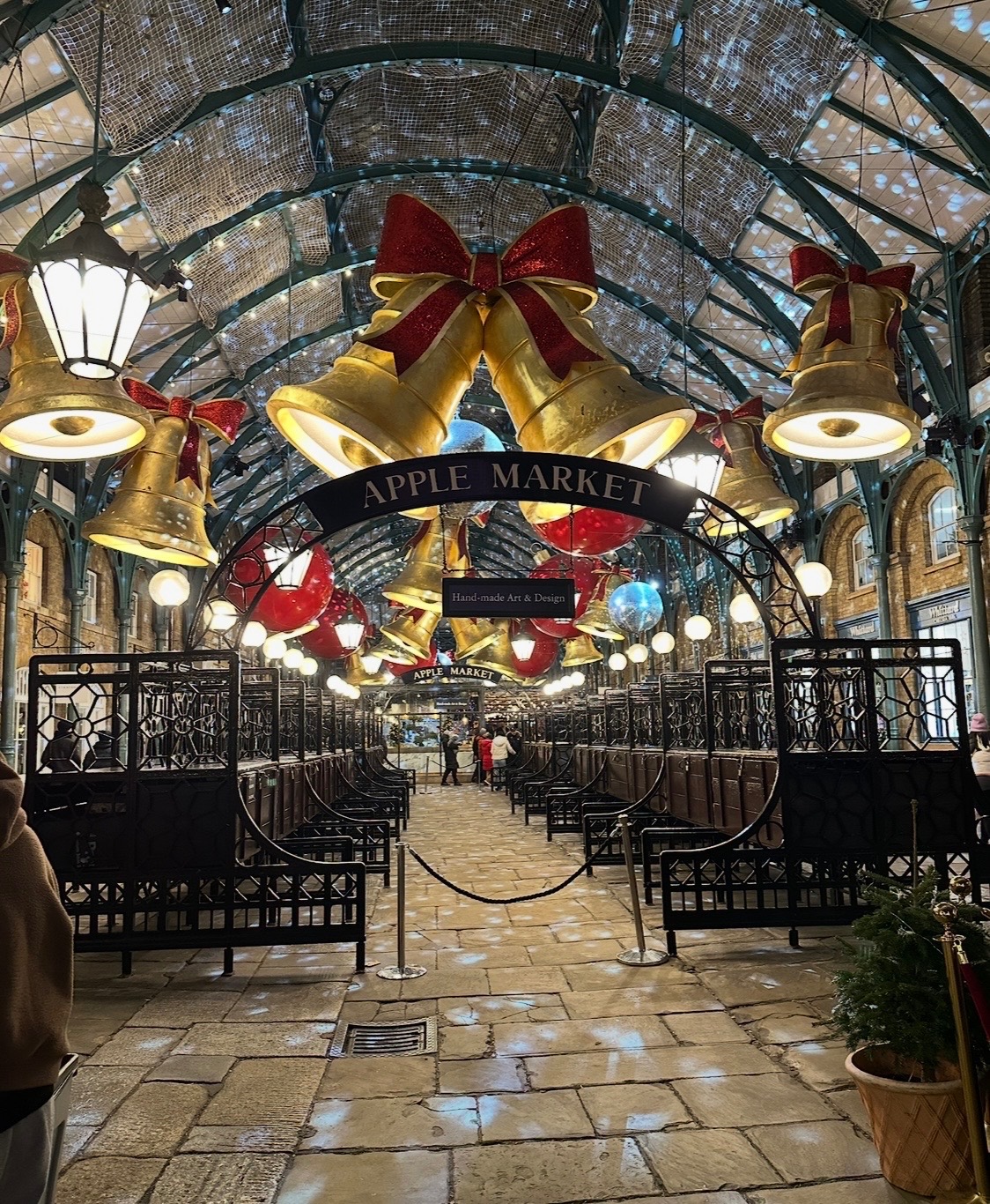Apple Market entrance with large golden bells adorned with red velvet bows and white lights strung overhead in a covered arcade