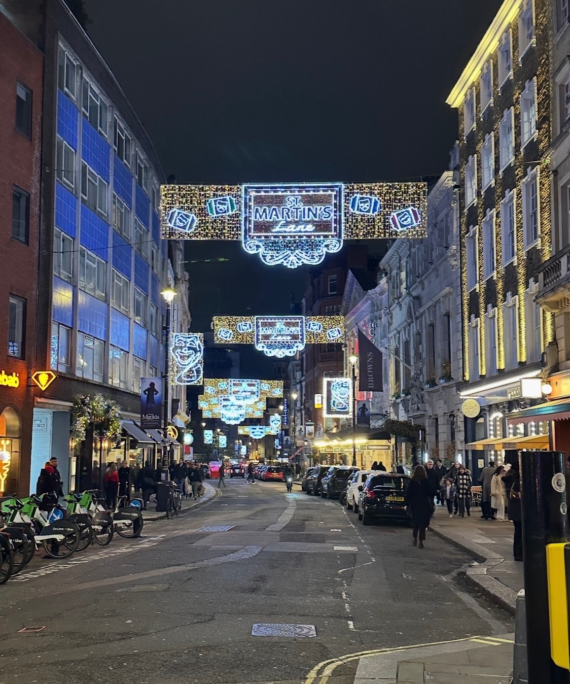Neon light display of a red bow and blue bird in a shopping arcade at night, with crowds of shoppers visible