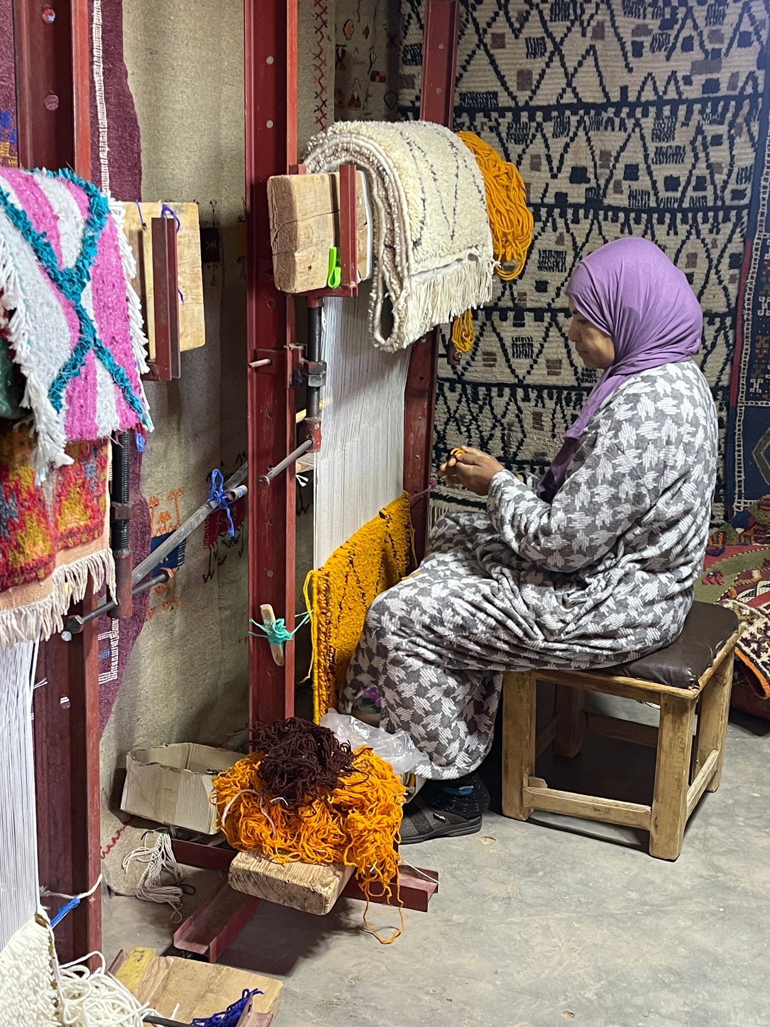 Woman working at a traditional loom weaving colorful Moroccan carpets and textiles