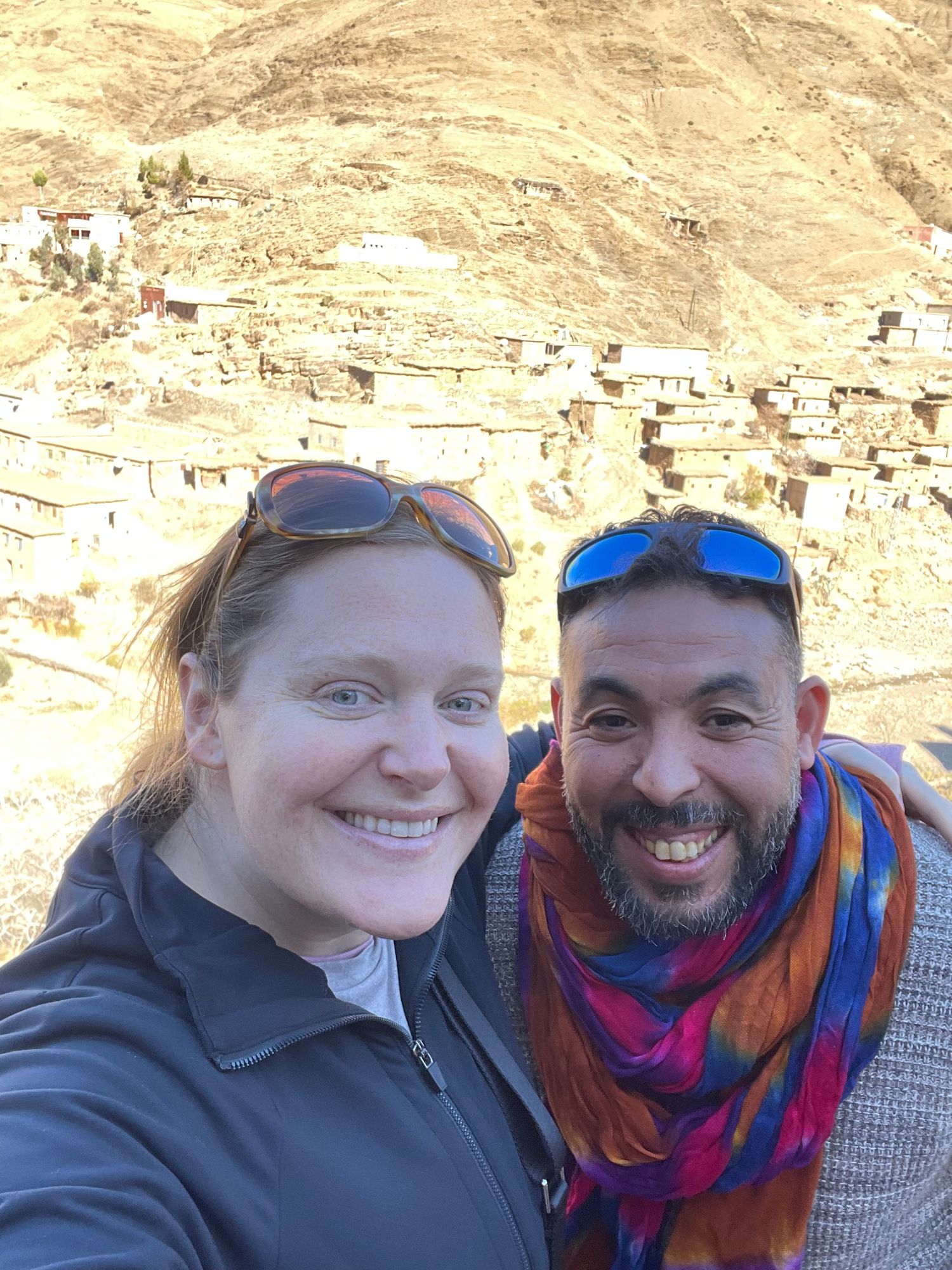 Katherine Friedman and a male companion smile for a photo with a Moroccan mountain village in the background