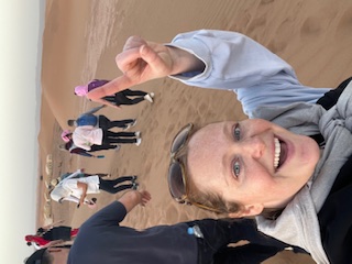 Katherine Friedman smiles at the camera during a desert excursion with group members visible in the background