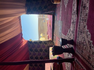 Interior view of a Berber tent with colorful rugs and cushions, looking out toward the desert