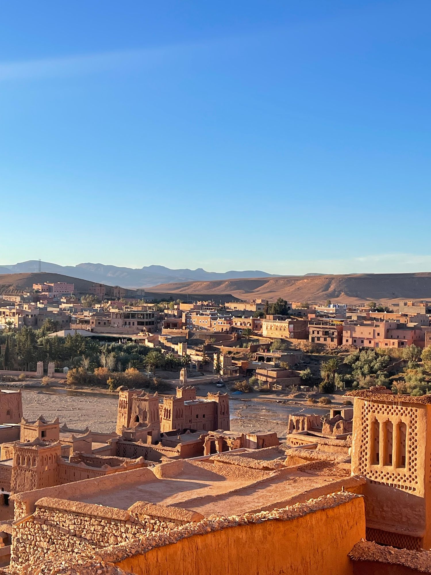 Panoramic view of a traditional Moroccan village with clay buildings nestled in a valley beside a river