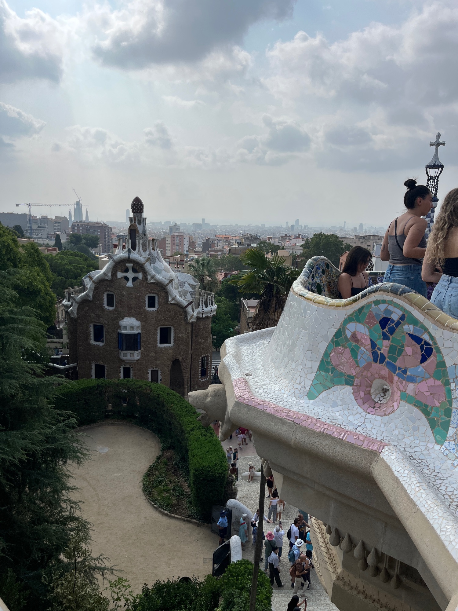 Park Güell's mosaic-covered terrace with colorful tile work overlooking Barcelona's cityscape and distant buildings