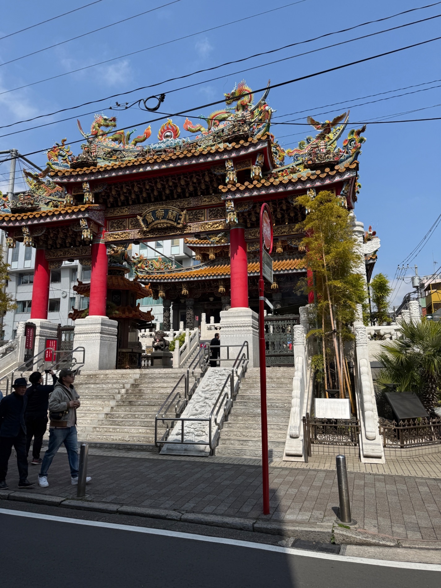 Ornate red and gold Chinese temple with multiple tiered roofs, dragons, and lanterns on a sunny day with people on the steps