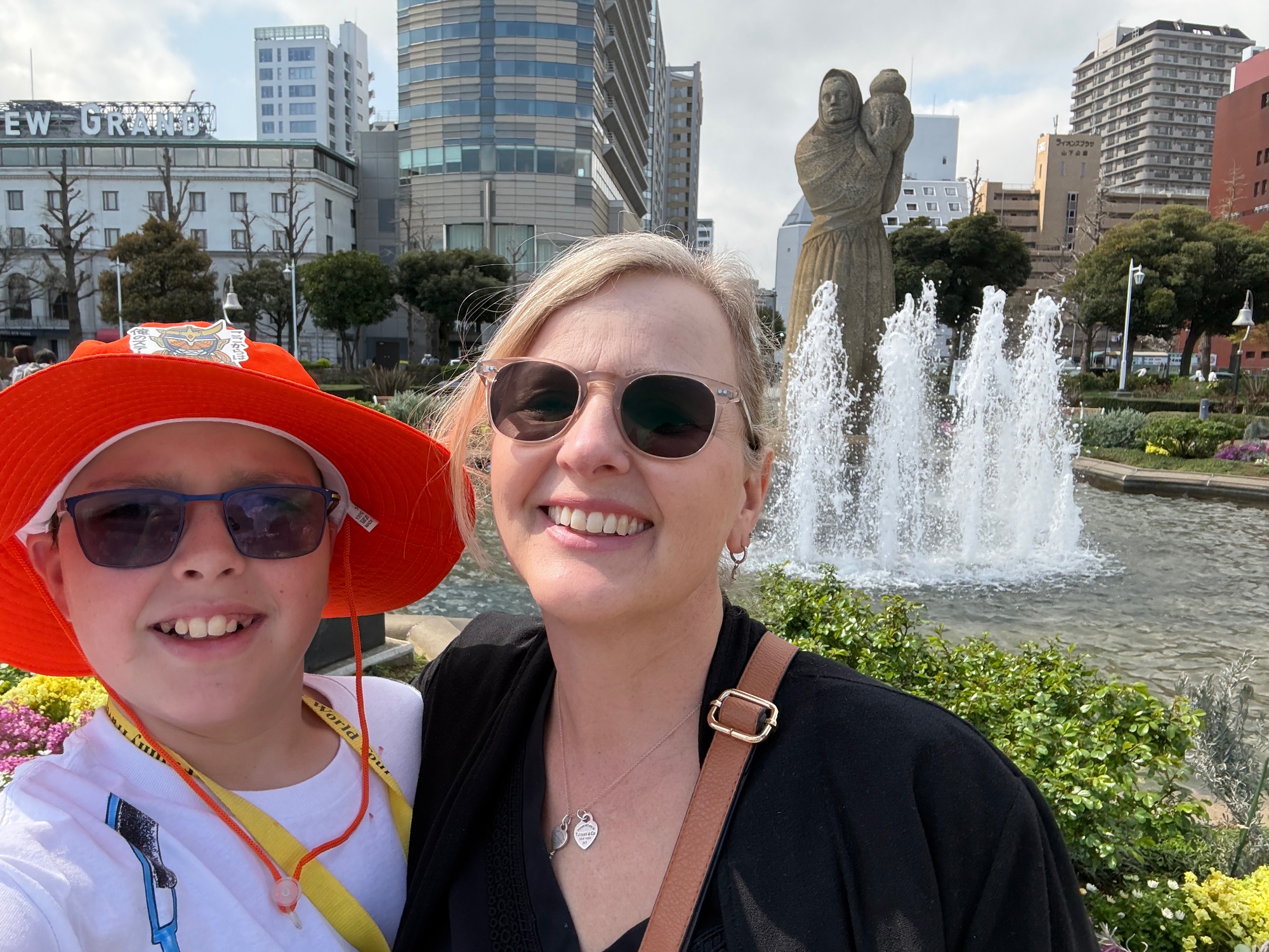 Marcia White and a young person smiling by a public fountain with a statue and city buildings in the background