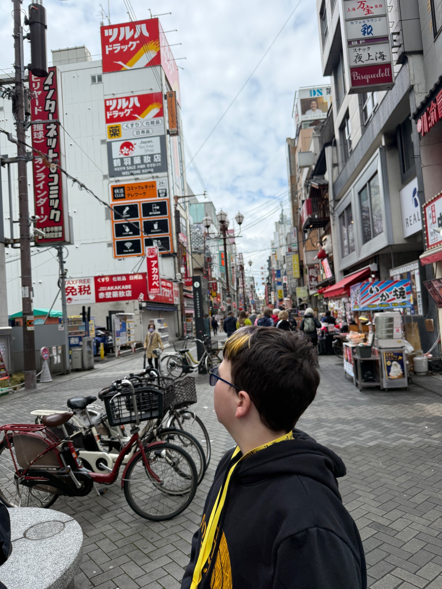 Young person walking on a busy Japanese shopping street lined with red signs, bicycles, and commercial storefronts