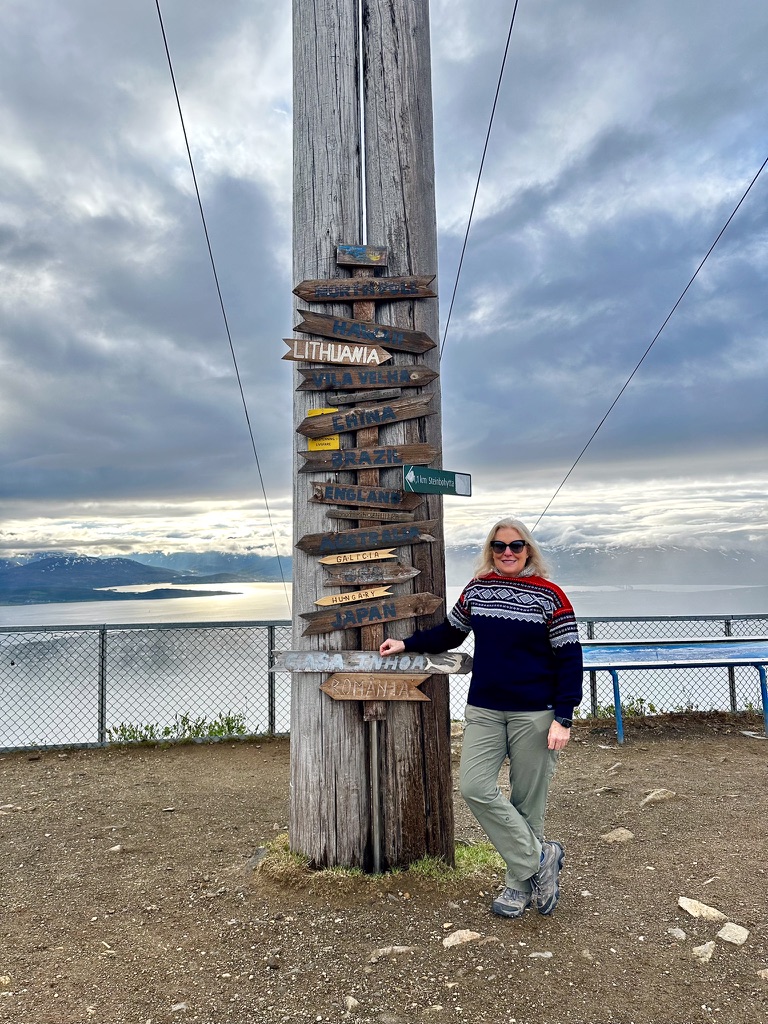 Woman posing next to wooden directional signpost with multiple destination signs on Arctic overlook