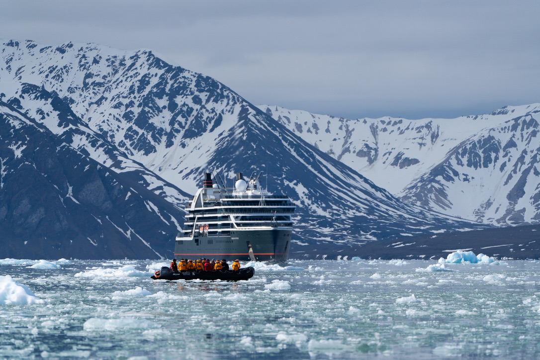 Woman in blue jacket on ship deck overlooking vast Arctic ice field from elevated position