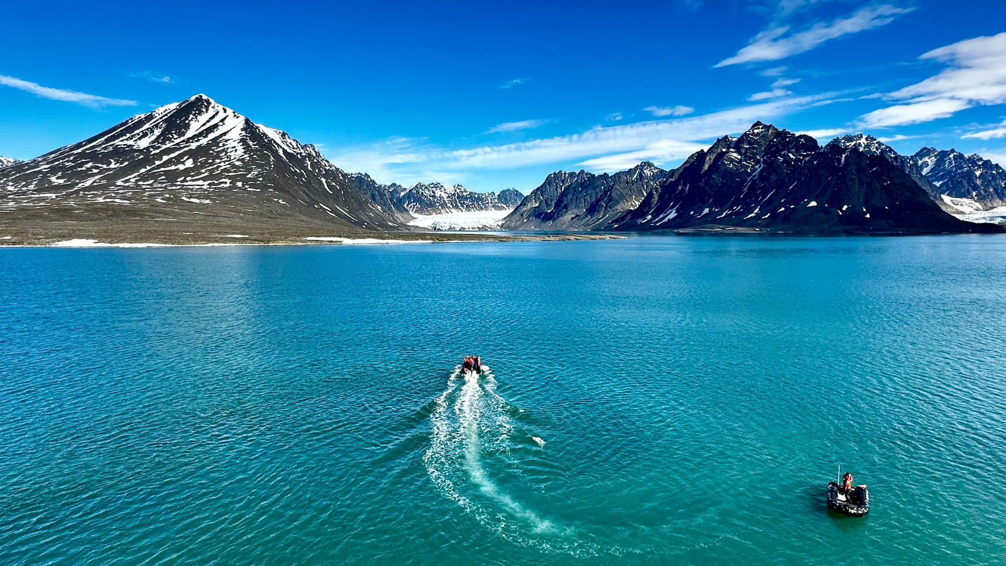 Woman in blue jacket standing on rocky shore of turquoise glacial lake with mountain peaks