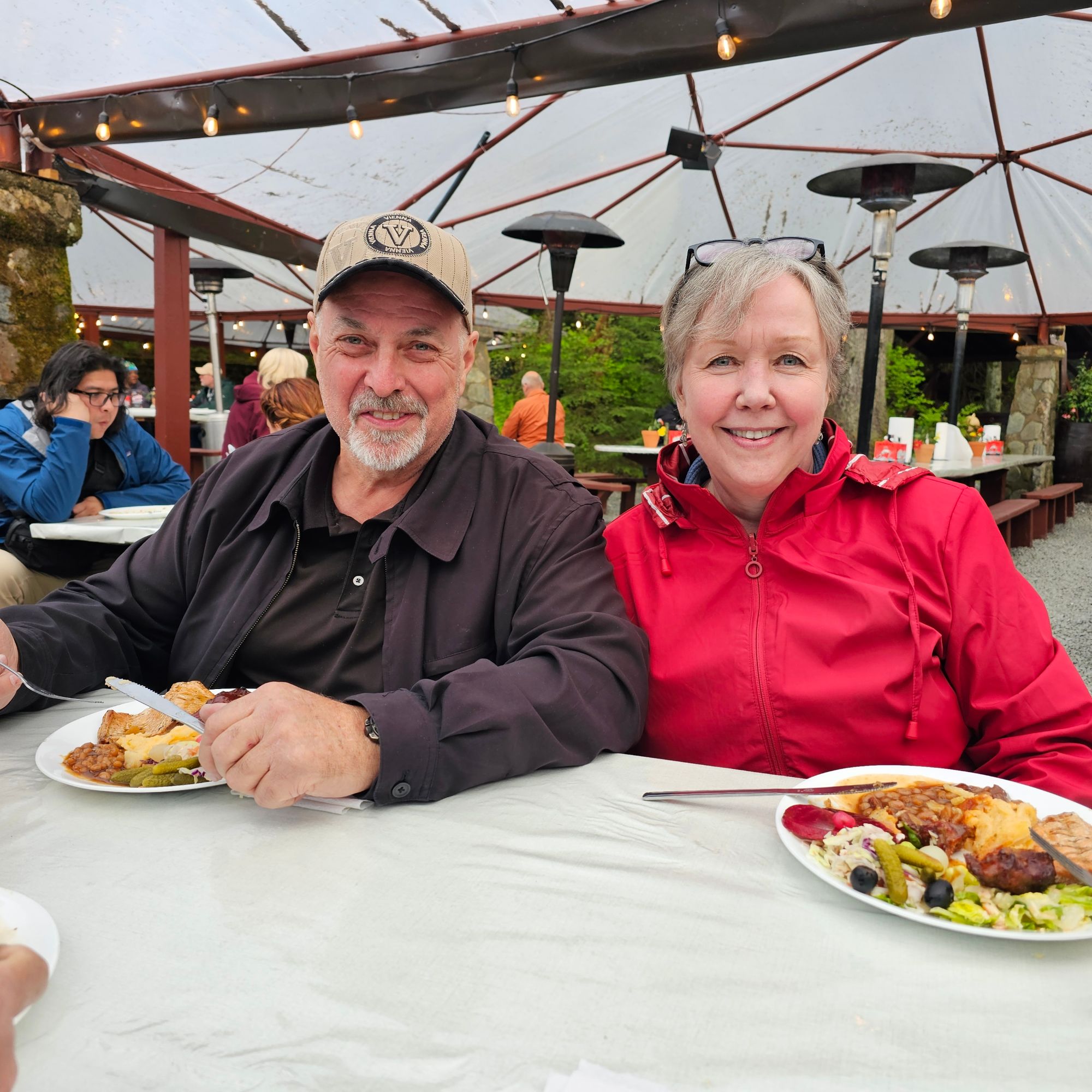 Lois Hirtz and a man enjoying grilled salmon and vegetables at an outdoor covered dining area in Alaska
