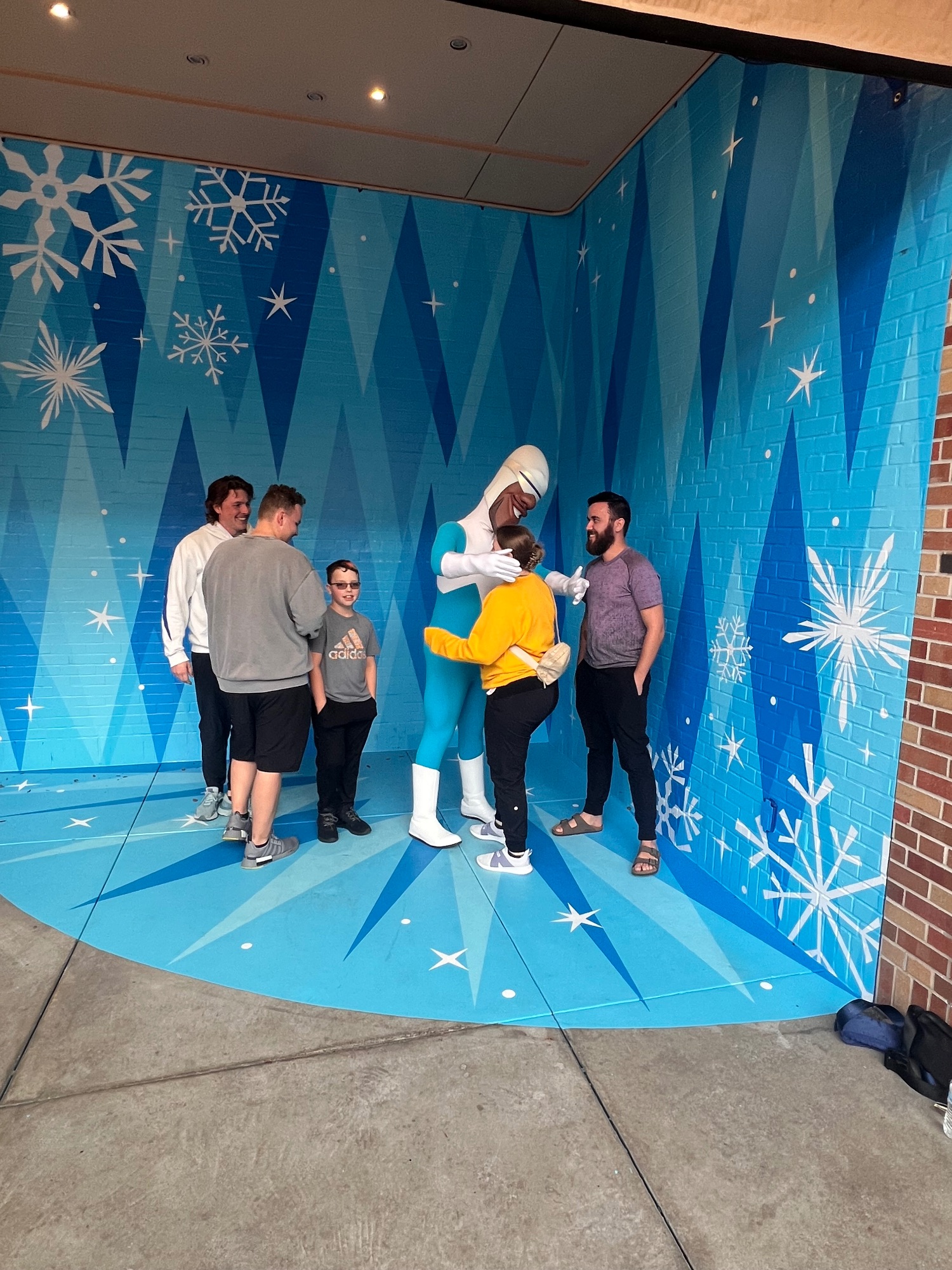 A group of five people stand in front of a blue snowflake-themed wall backdrop with winter decorations at a theme park