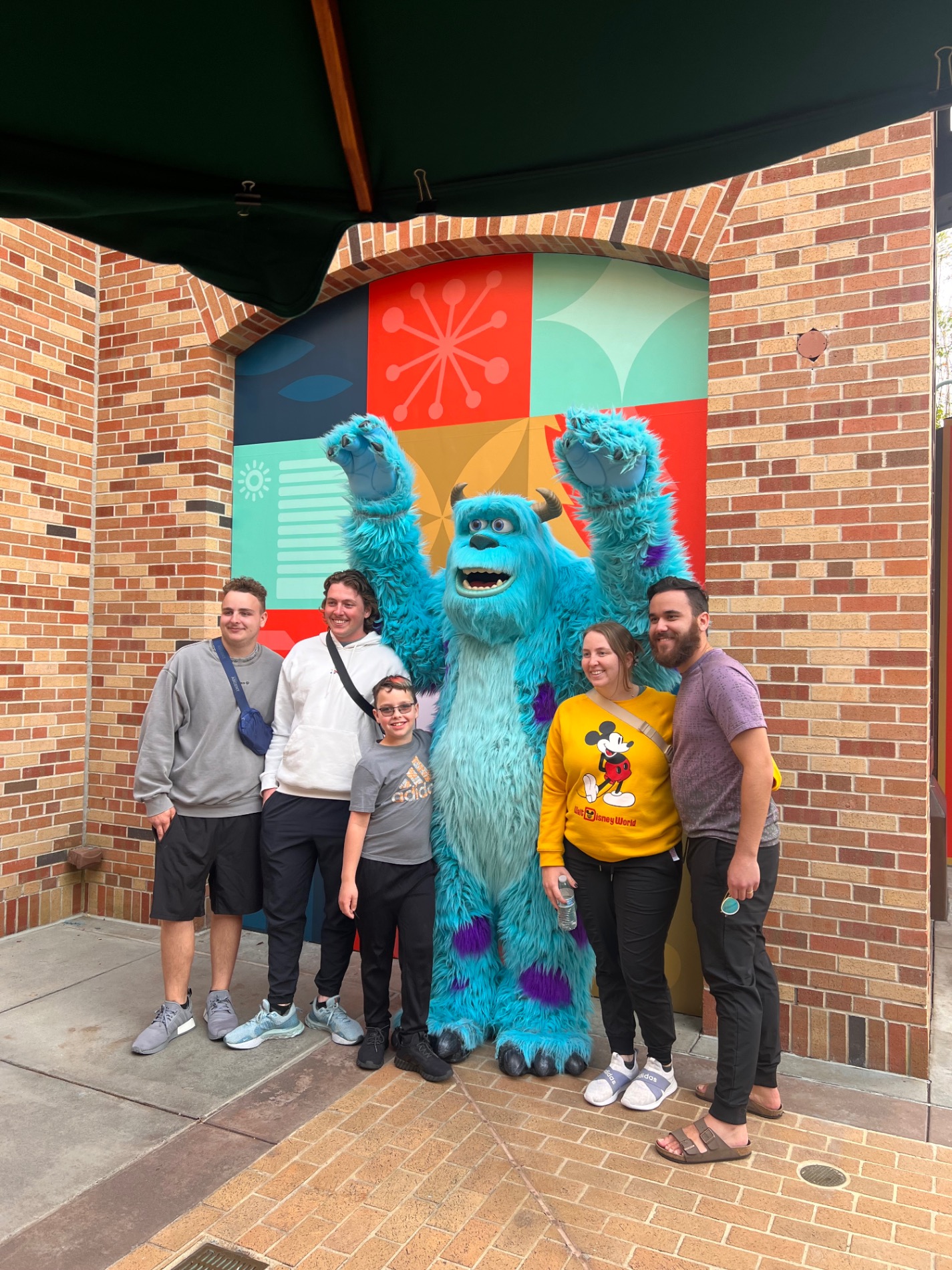 A family of five poses with a large blue furry character costume at a theme park outdoor location