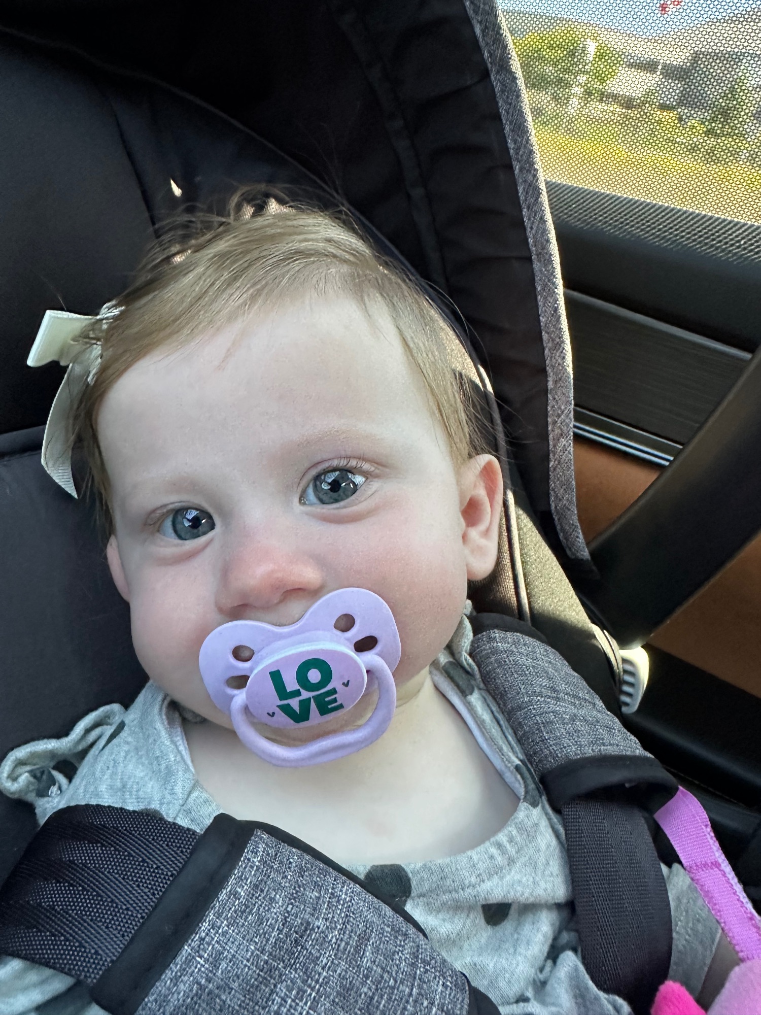 Close-up of a baby with a pacifier that says 'LOVE' in a car seat