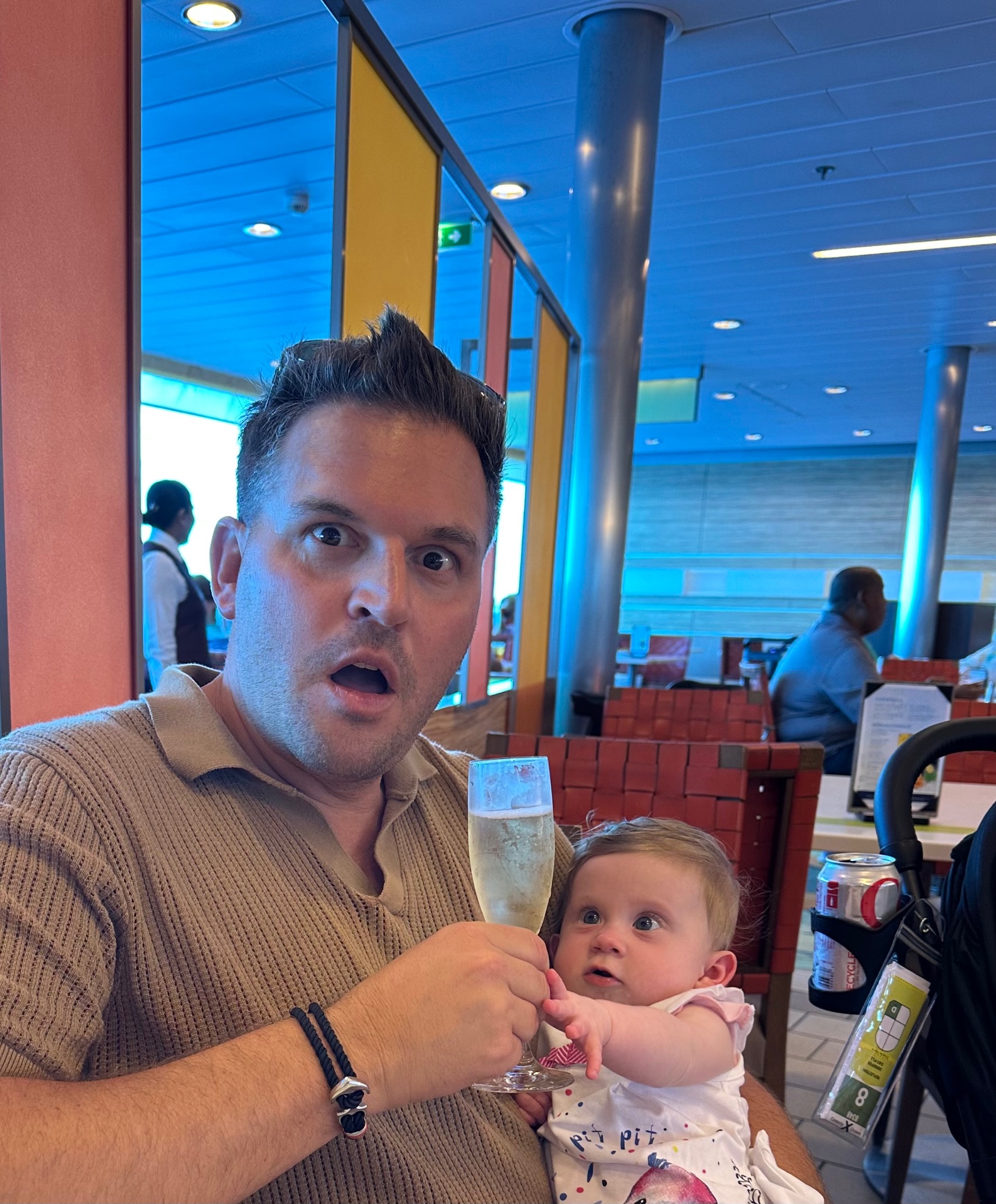 Two men with a baby in a stroller at a waterfront dock with turquoise water