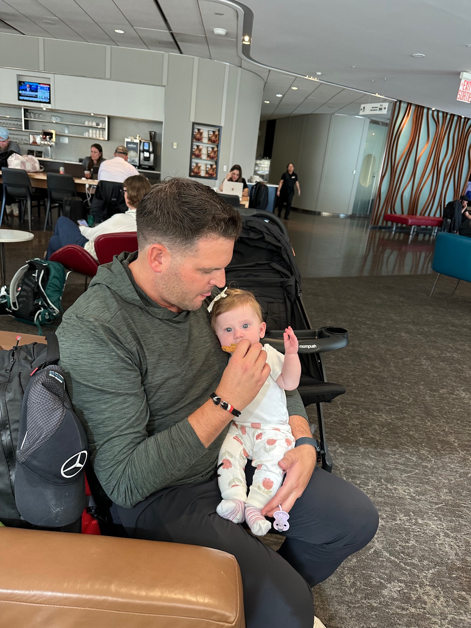 Man holding a baby while sitting in an airport lounge with other passengers