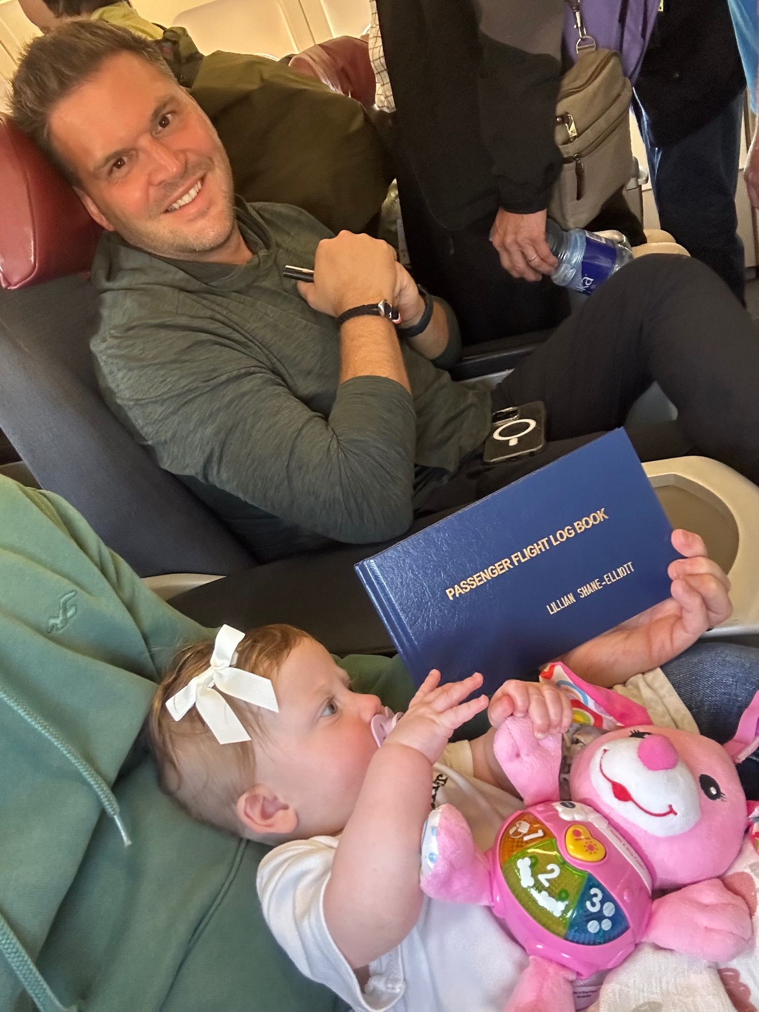 Man in a plane seat holding a baby and showing a passenger flight log book