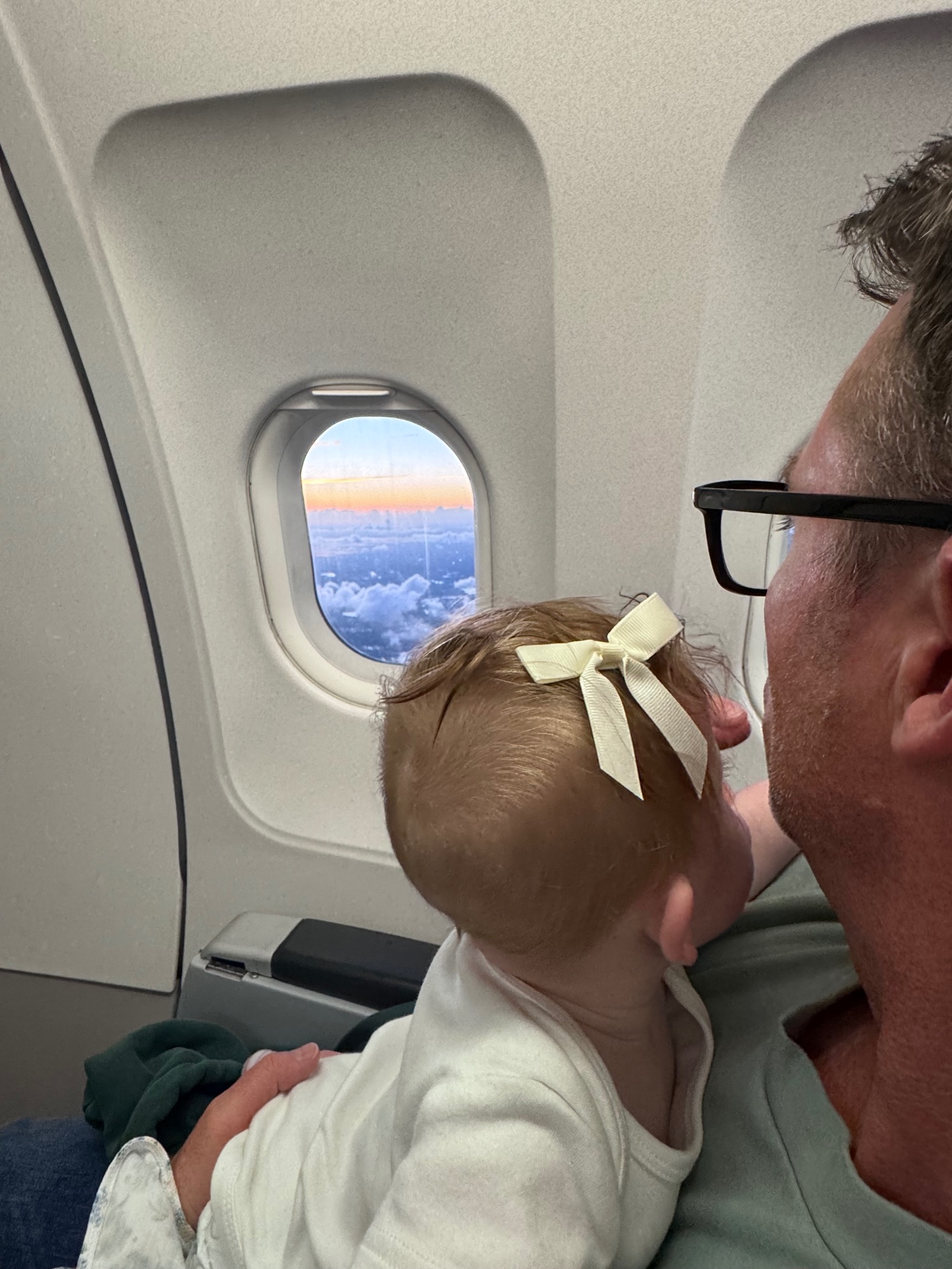 Baby looking out an airplane window at clouds and sky during flight