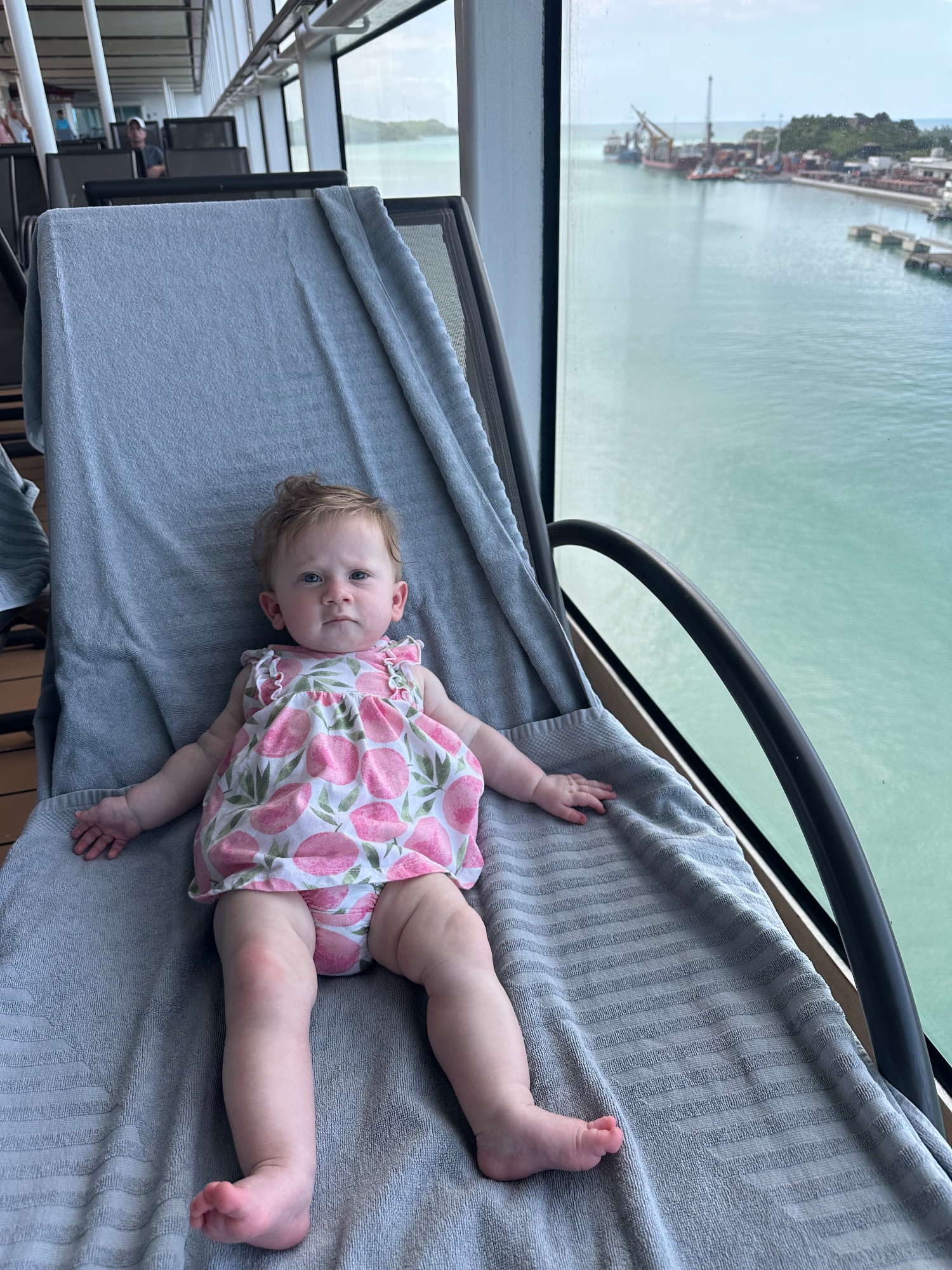 Baby in a stroller on a cruise ship deck with ocean and port infrastructure visible