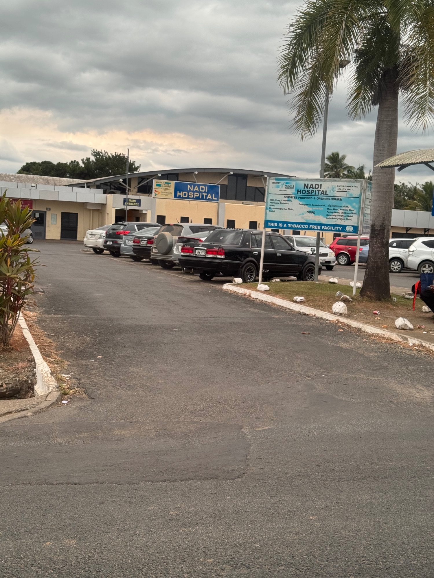 Nadi Hospital building with parking lot and palm trees under cloudy sky