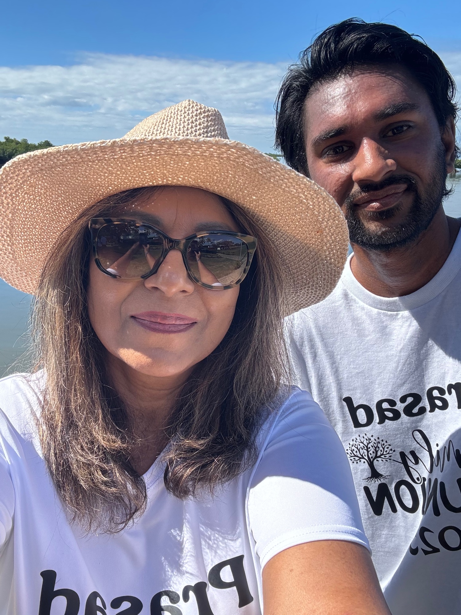 Woman and man in casual clothing posing together outdoors with blue sky and water behind them