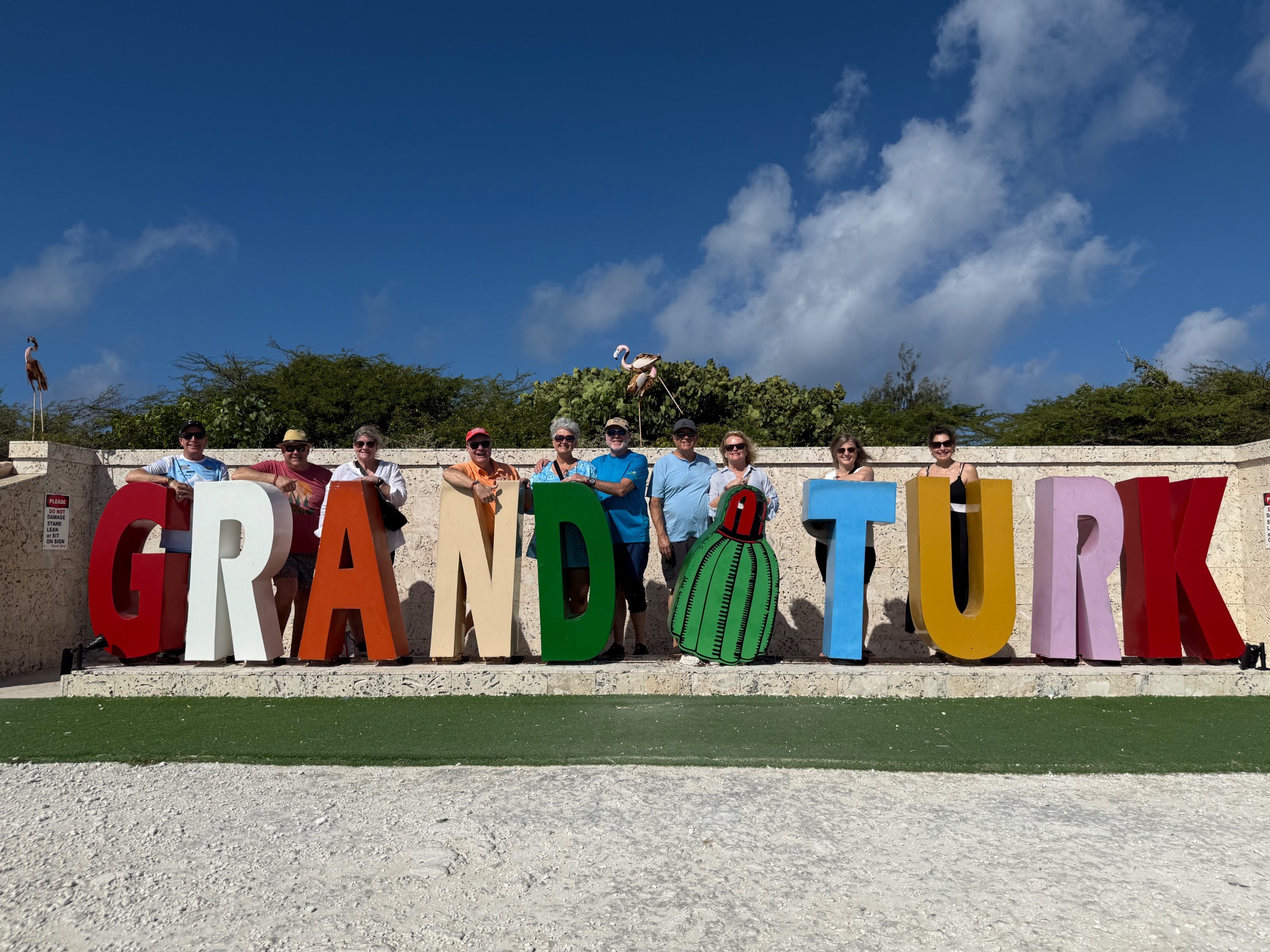 Large colorful GRAND TURK sign with group of tourists posing behind the letters in bright sunlight
